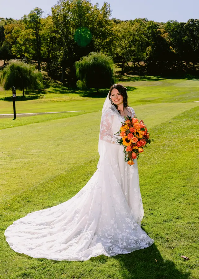 Bride Wearing Lace Long Sleeve Aline Wedding Dress Called Winter By Maggie Sottero Holding Orange And Yellow Bouquet
