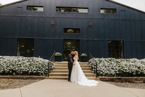 Bride Wearing Aline Satin Wedding Gown Called Scarlet By Maggie Sottero Kissing Groom In Front Of A Black Building