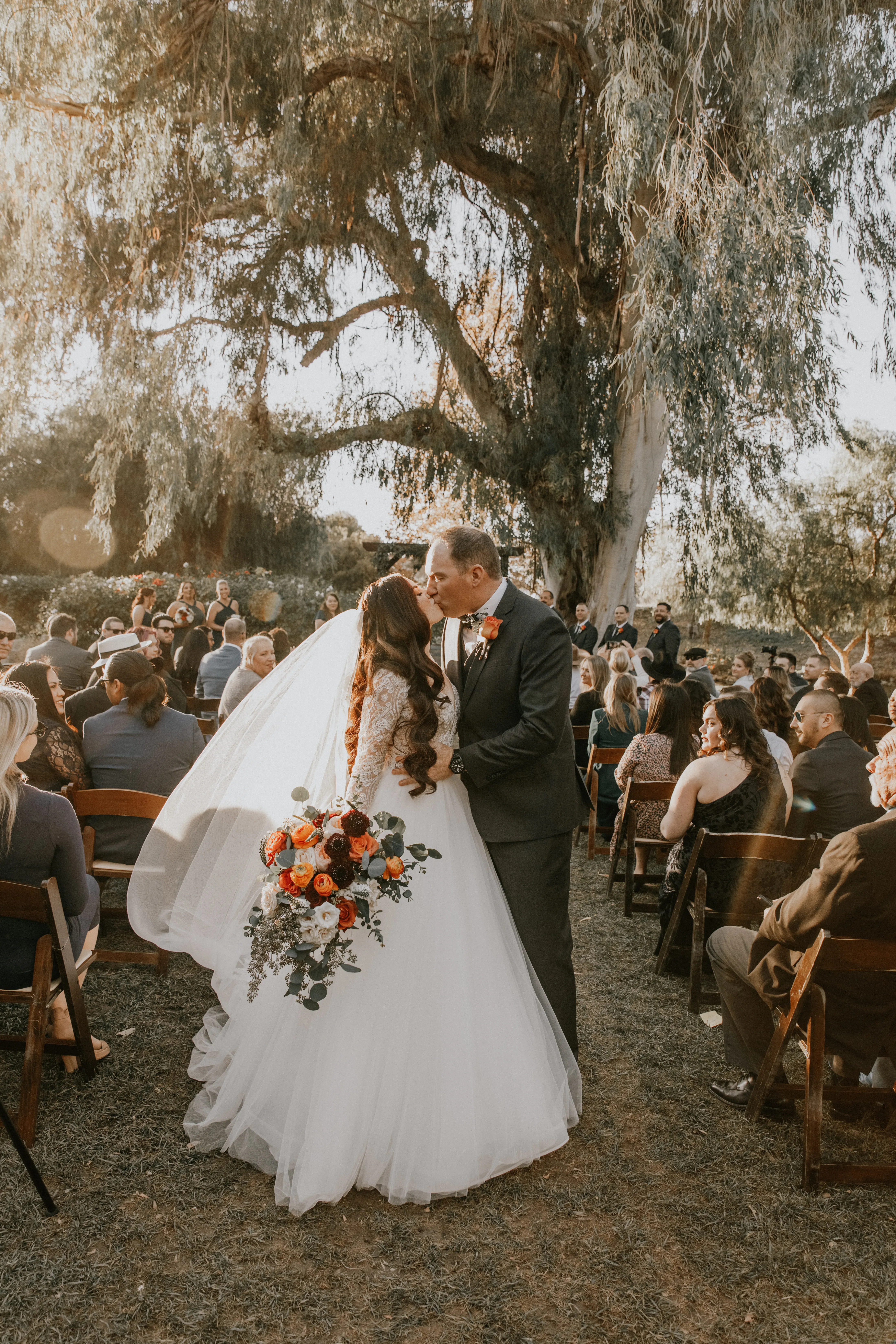 Groom And Bride Share Kiss In Aisle. Bride Wearing Tulle Long Sleeve Ball Gown Called Mallory Dawn By Maggie Sottero