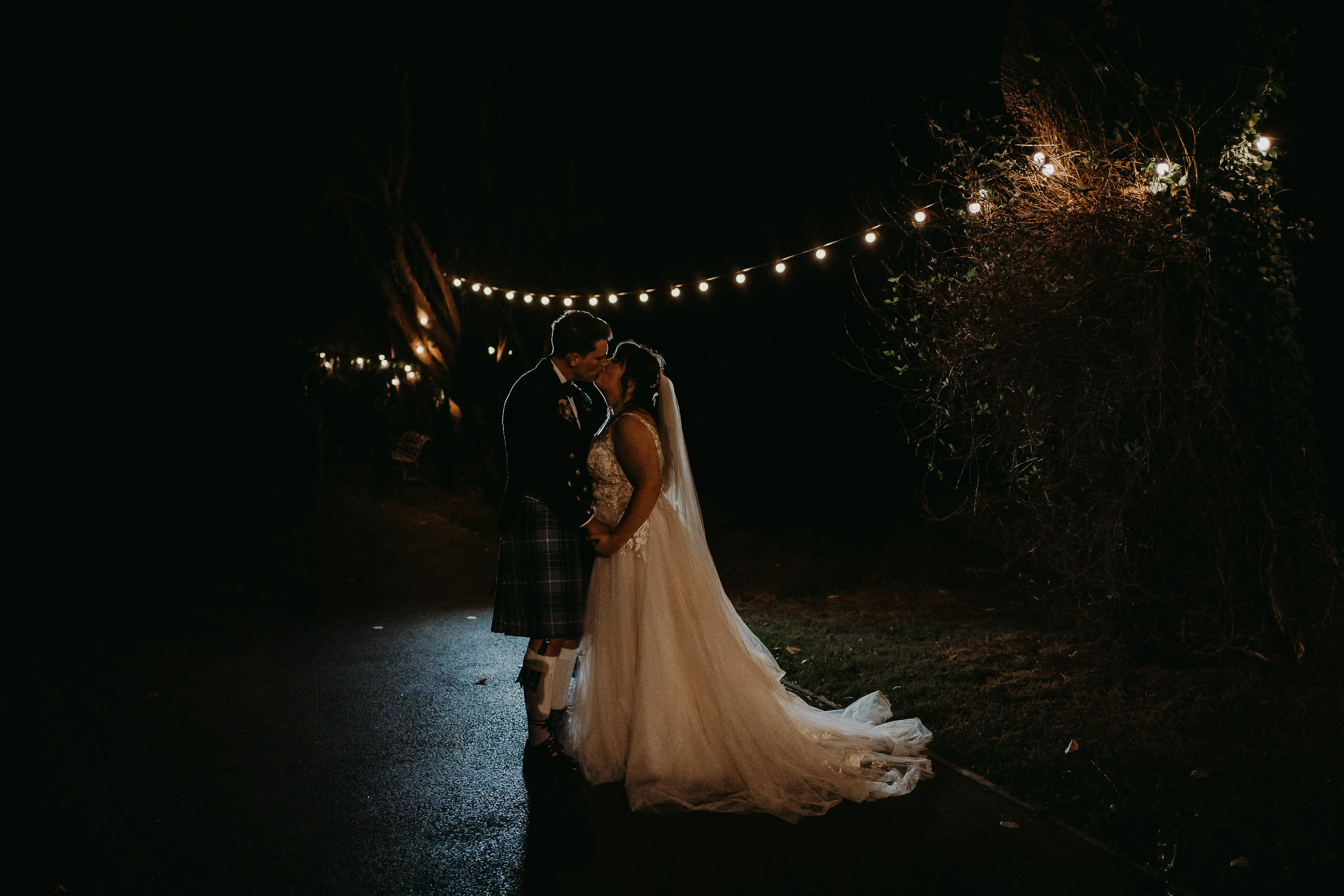 Bride and groom kissing under fairylights.