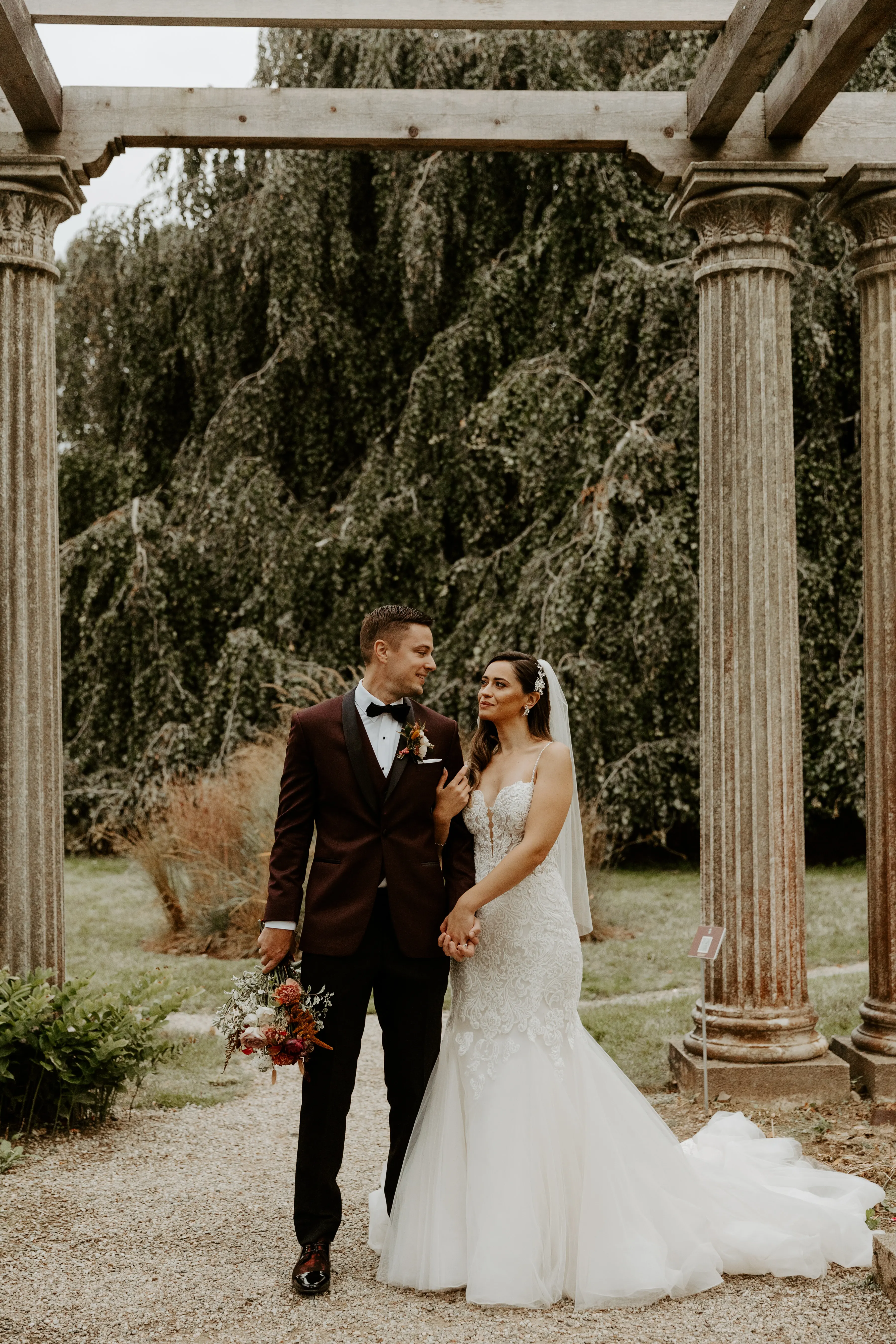 Bride with groom wearing lace fit-and-flare wedding dress holding bridal bouquet outdoors.