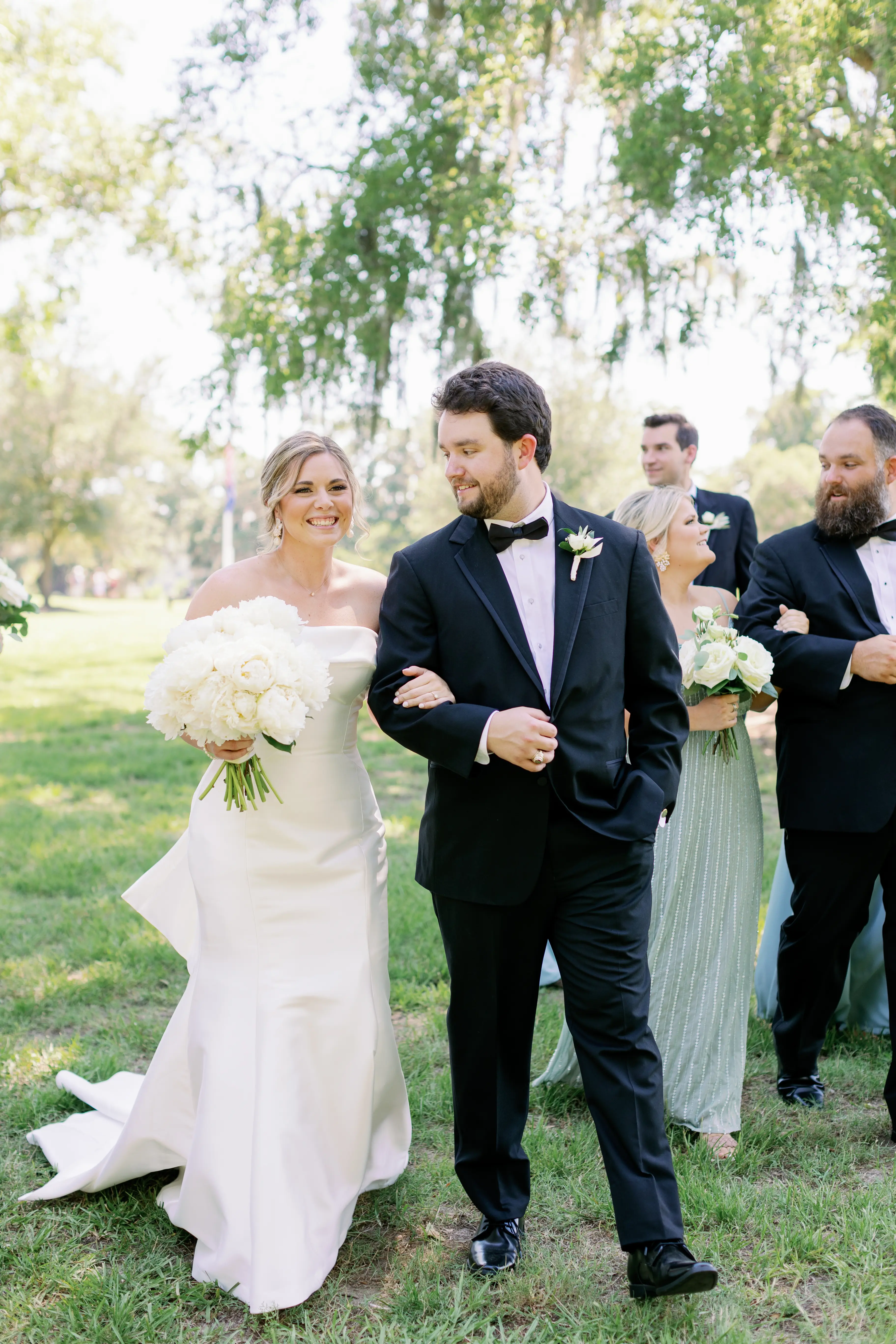 Bride with groom wearing strapless elegant mermaid wedding dress outdoors holding flower bouquet.