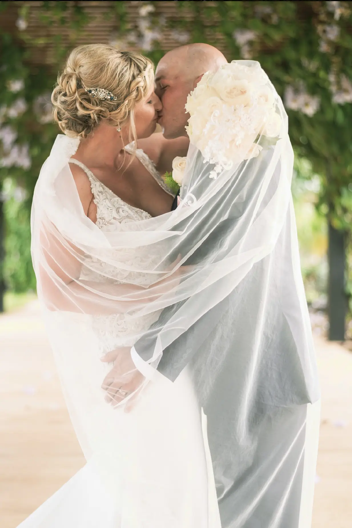 Couple kissing while bride wraps her veil around her groom.