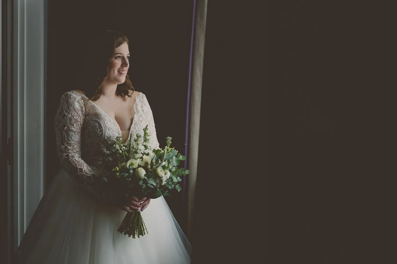 Bride Wearing Dreamy Long Sleeve Ballgown Wedding Dress Called Mallory Dawn By Maggie Sottero Looking Out Window Holding Bouquet
