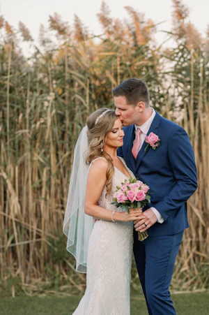Groom kissing his bride in front of tall grass.