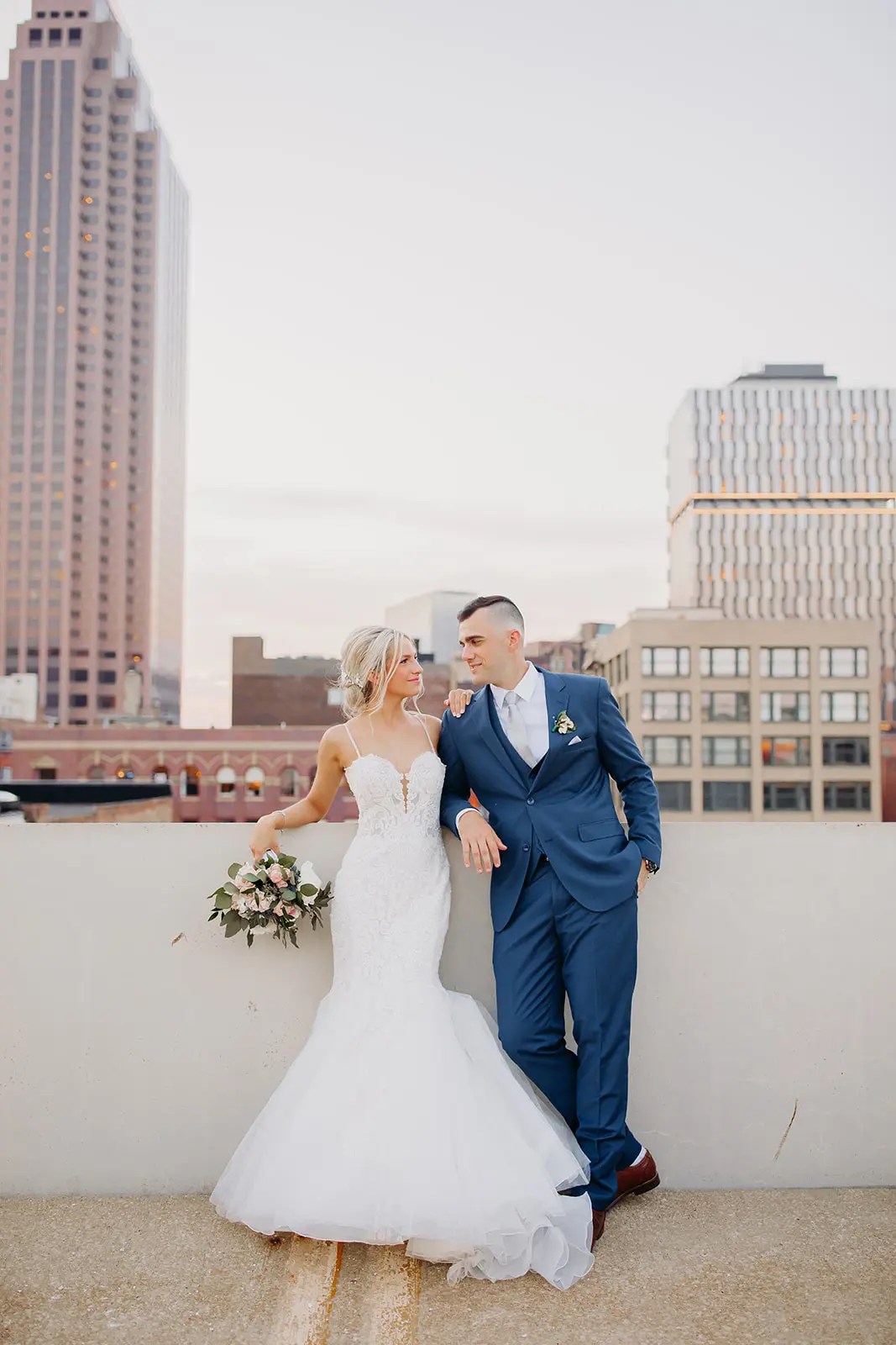 Bride and groom looking at each other with view of buildings behind them.
