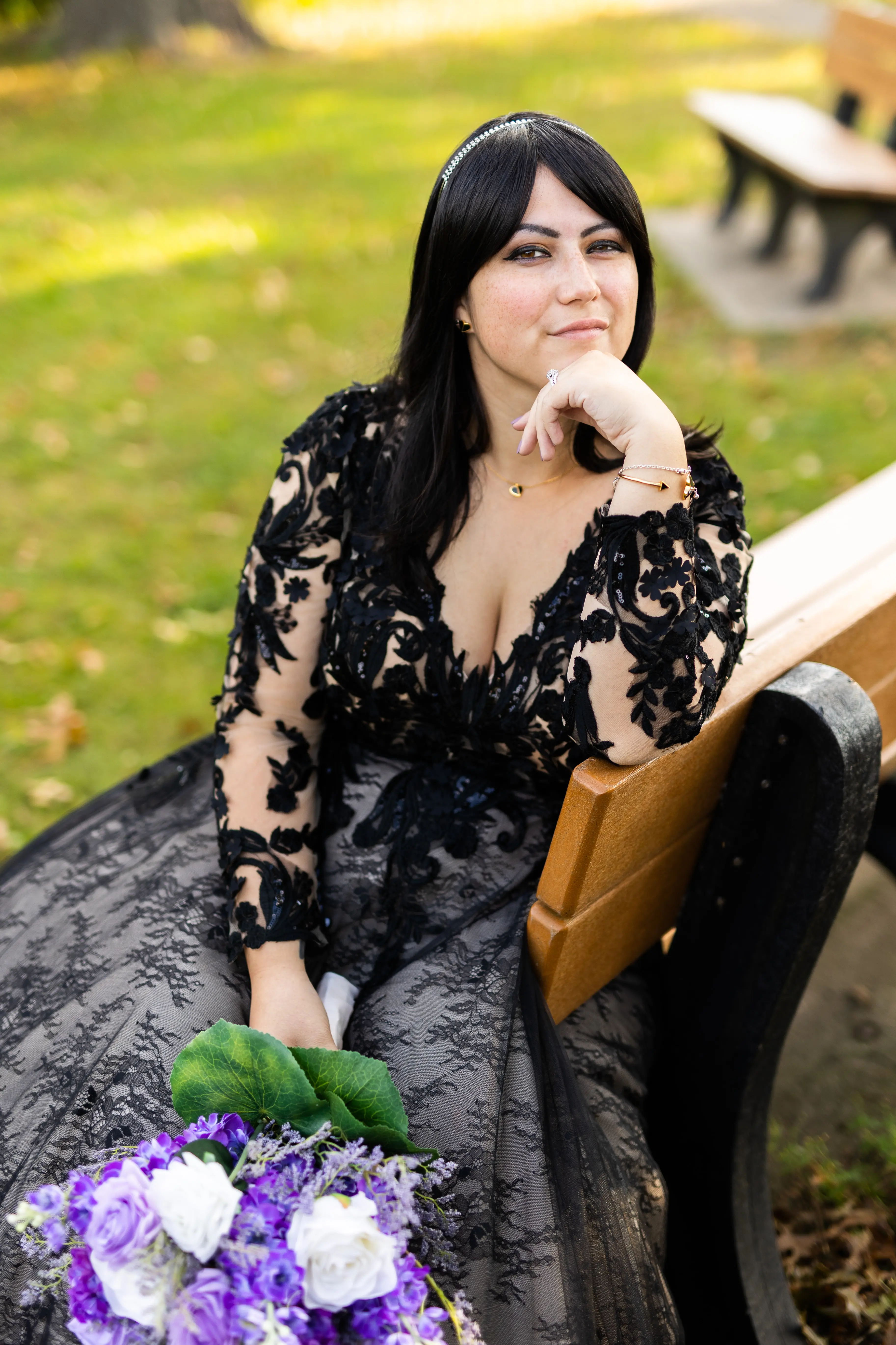 Bride Sitting Down Wearing Long Sleeve Black Lace Ballgown Wedding Dress Holding Bridal Bouquet.