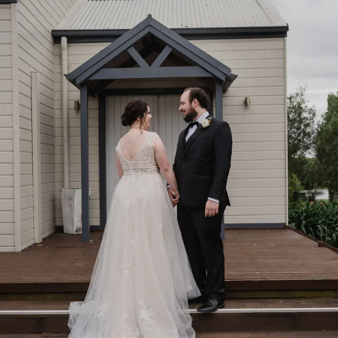 Groom Holding Hands with Bride in V-Back Wedding Dress Raelynn by Rebecca Ingram
