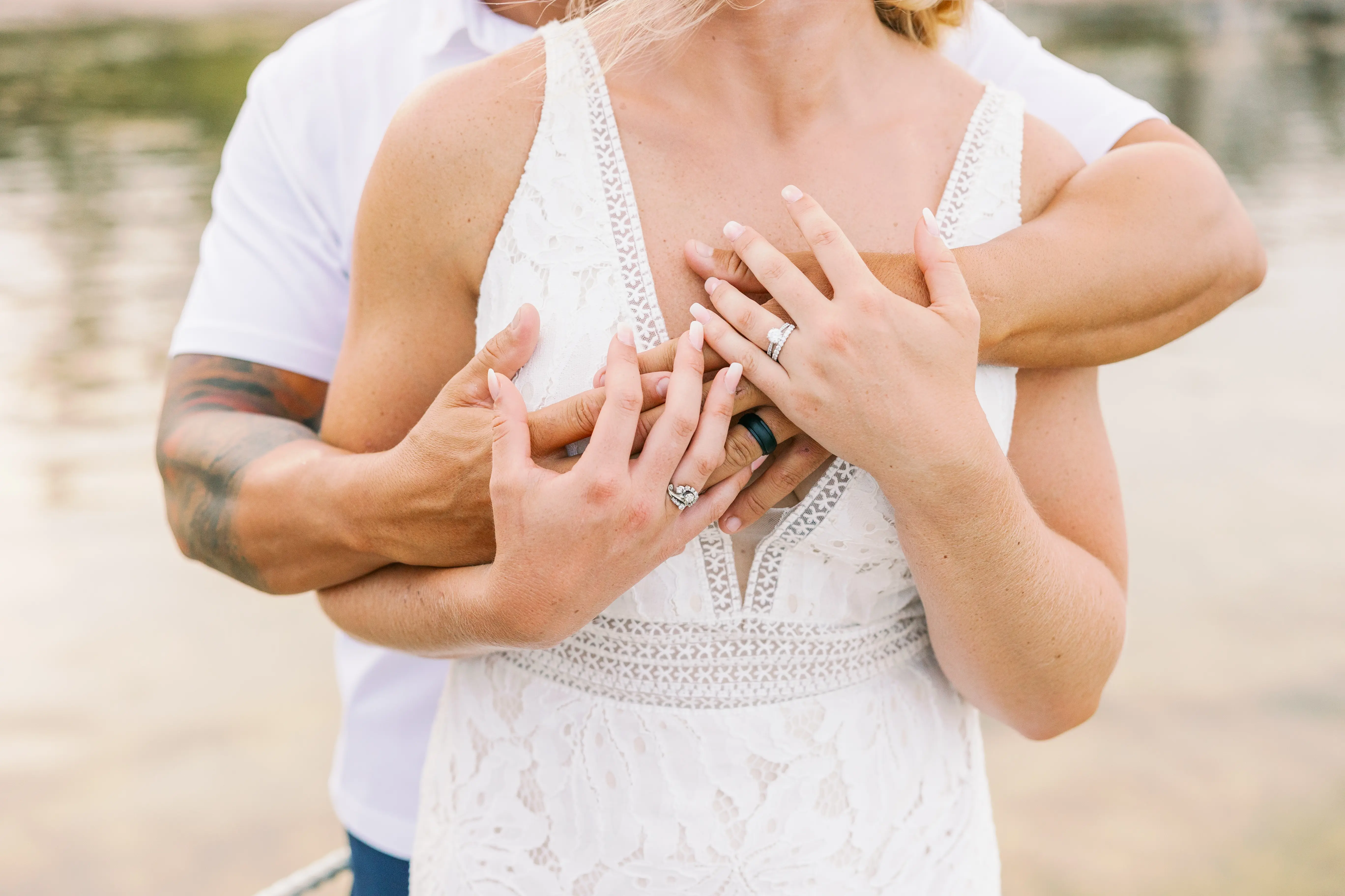 Closeup of newlyweds rings as groom embraces bride from behind.