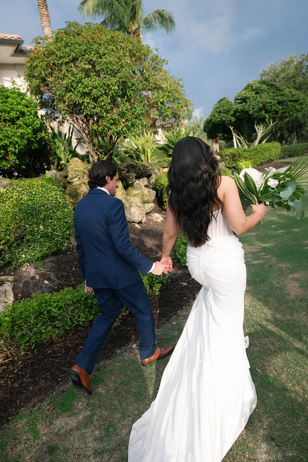Bride Wearing Grecian Inspired Wedding Dress Called Gabrielle By Maggie Sottero Walking With Groom In A Garden