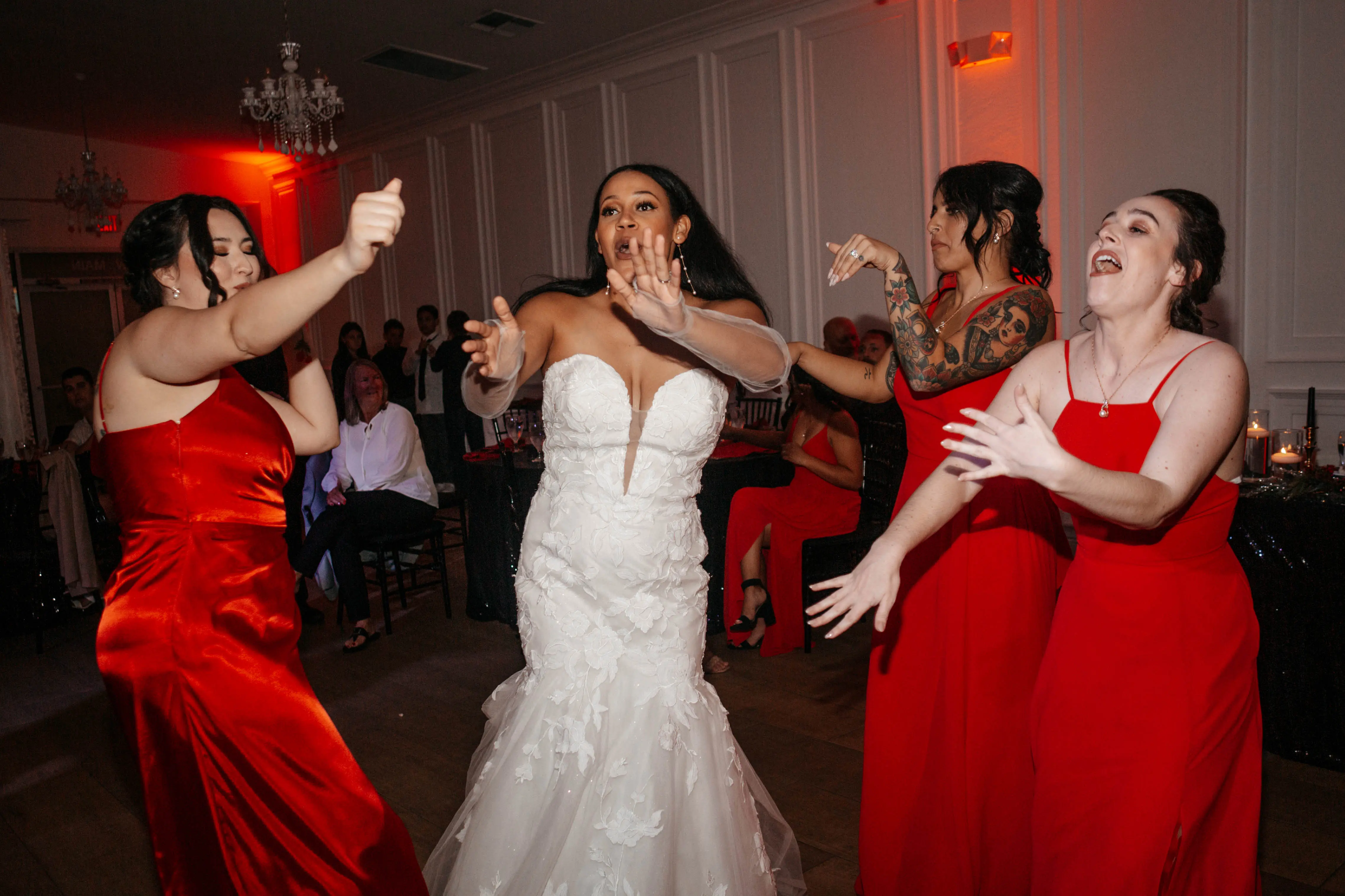 bride in plunge neckline wedding dress called hattie by rebecca ingram with bridesmaids in red