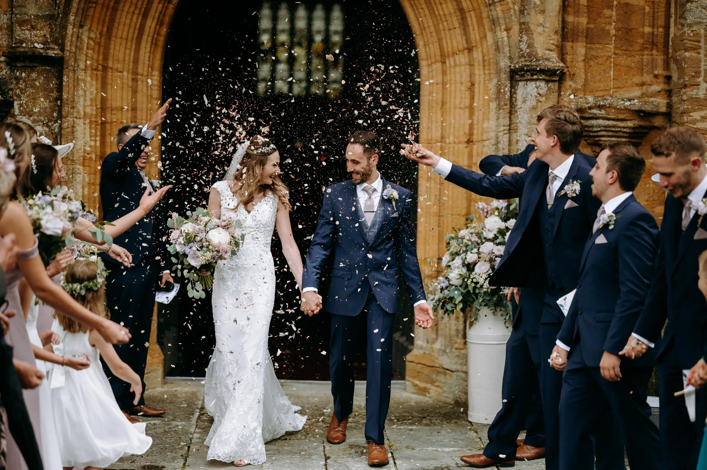 Confetti throw outside church. Bride and groom looking at each other laughing.