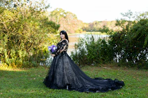 Bride in a Field Wearing Long Sleeve Black Lace Ballgown Wedding Dress Holding Bridal Bouquet.