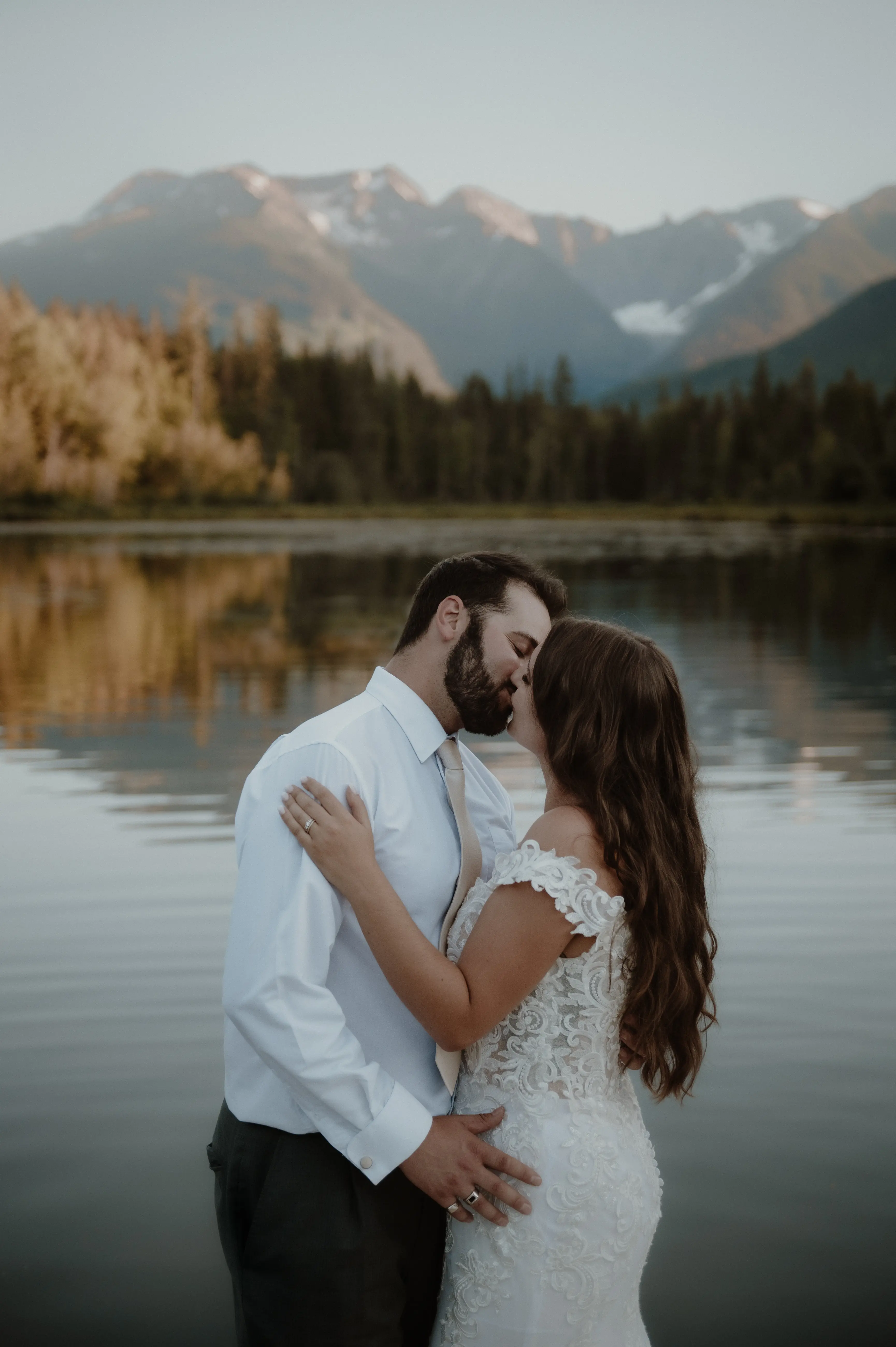 Bride with groom wearing romantic lace off-the-shoulder wedding dress outside in the mountains.