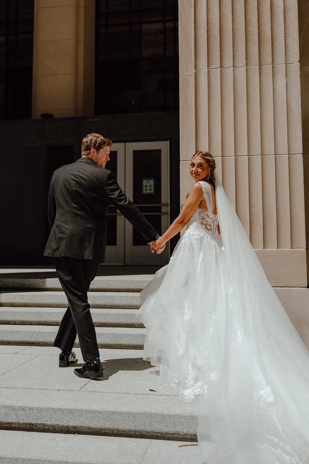 Bride Wearing Floral Ethereal Tulle Wedding Dress Called Lettie By Rebecca Ingram Holding Hand With Groom Outside