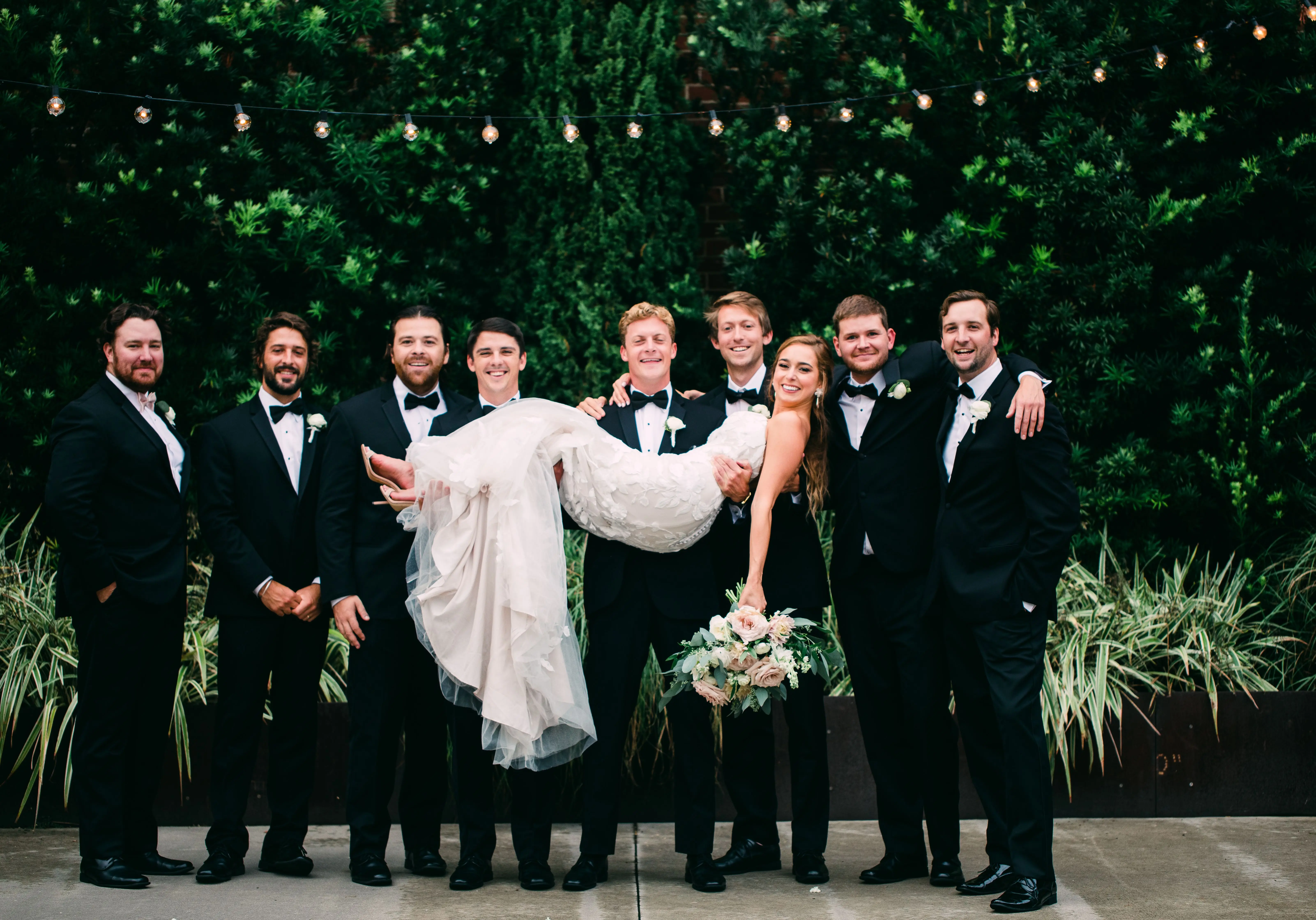 Bride with groomsmen wearing strapless mermaid wedding dress with oversized lace
