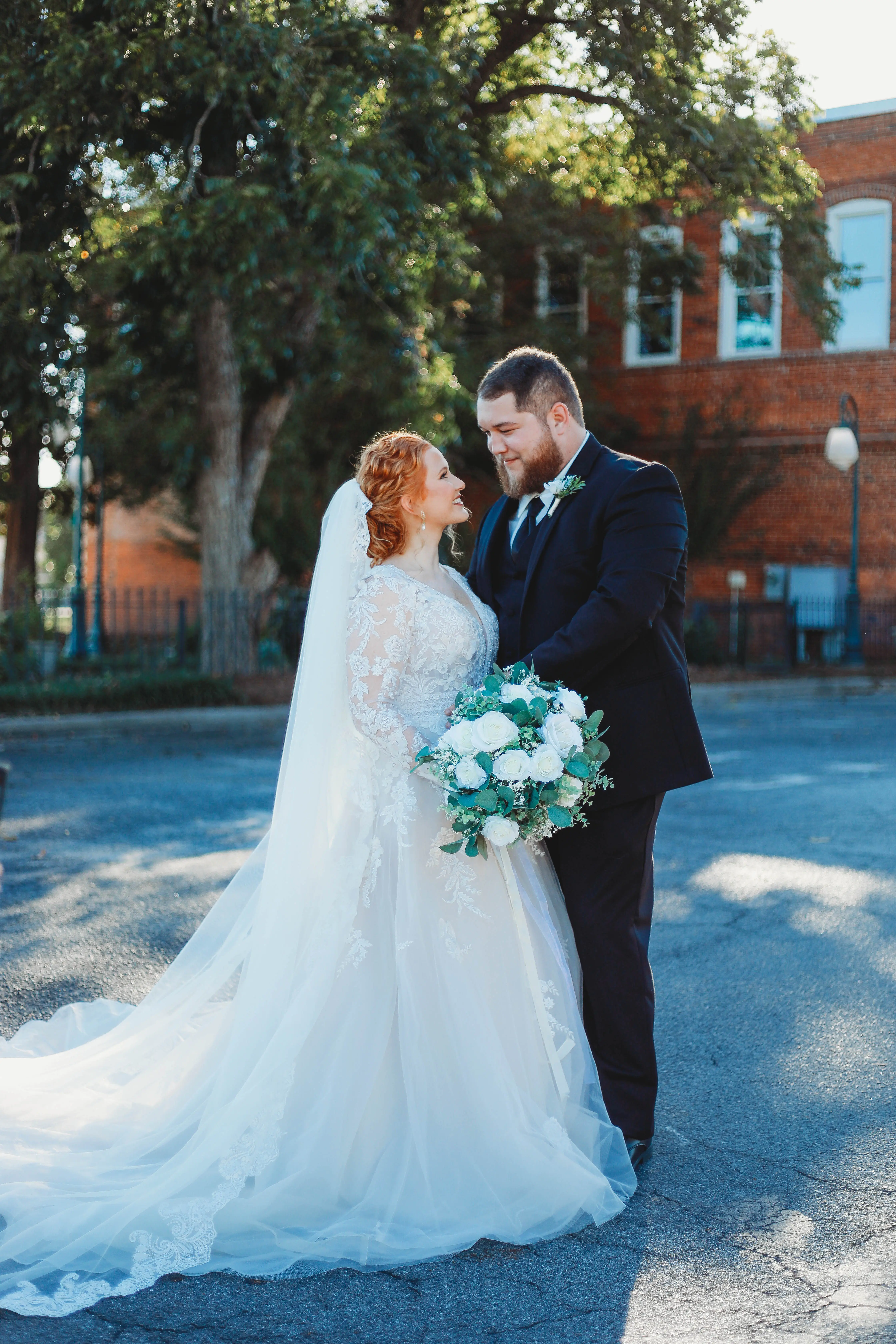 Bride And Groom Standing Together. Bride Wearing Illusion Sleeve A-line Wedding Dress Called Raphael By Maggie Sottero With Cathedral Veil