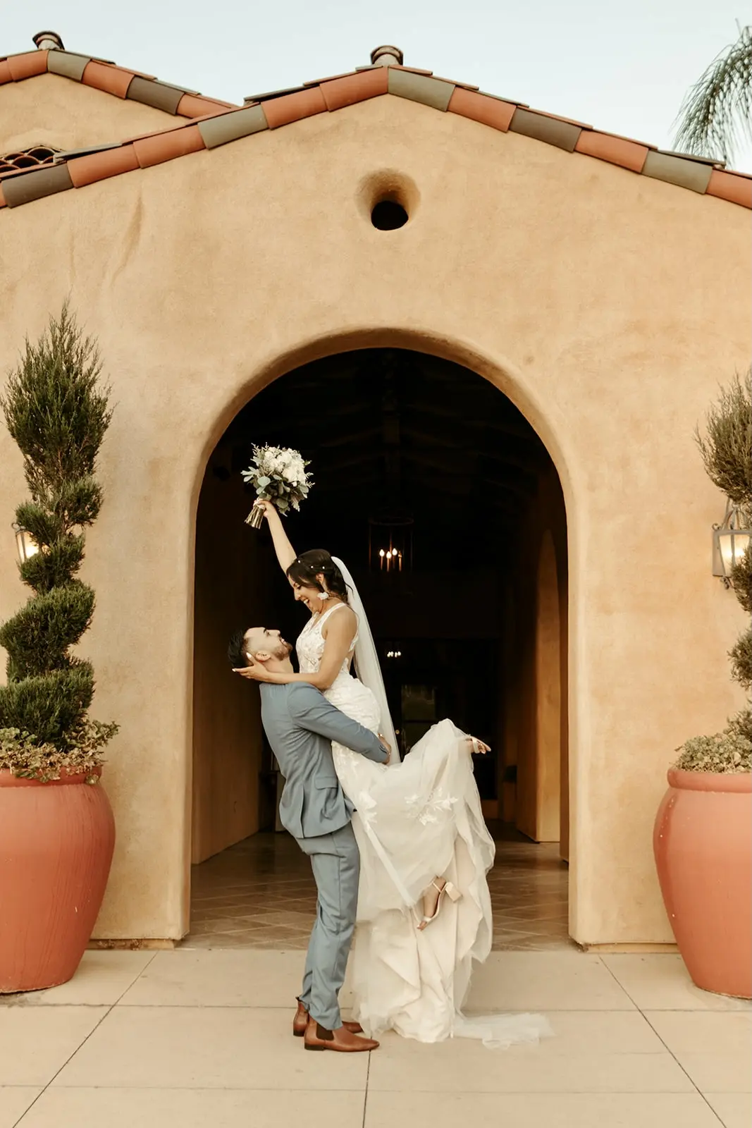 Groom lifting his smiling bride who is wearing wedding dress called Elizabetta.