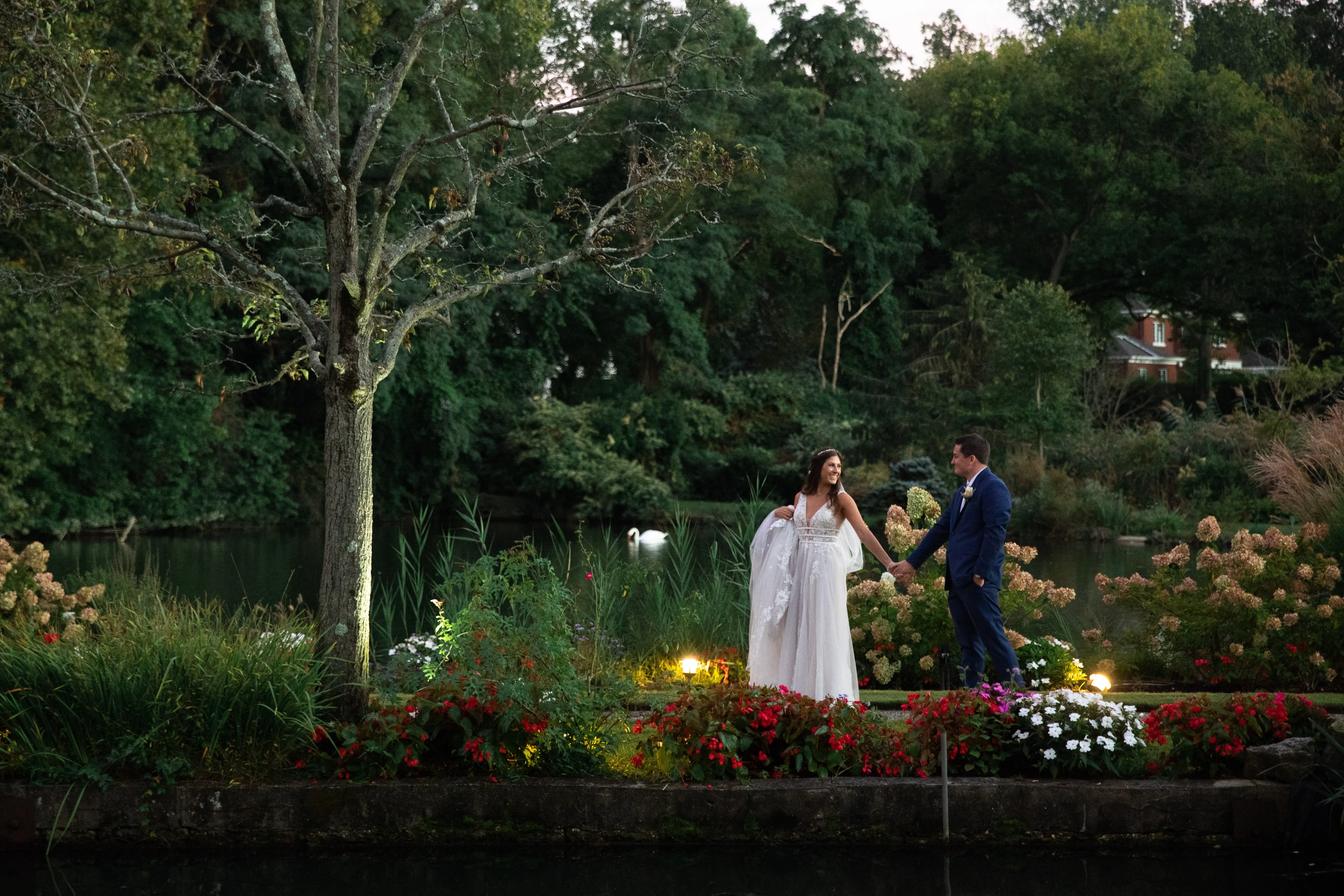 wearing Lace A-line Wedding Dress called Raelynn by Rebecca Ingram and groom in a garden