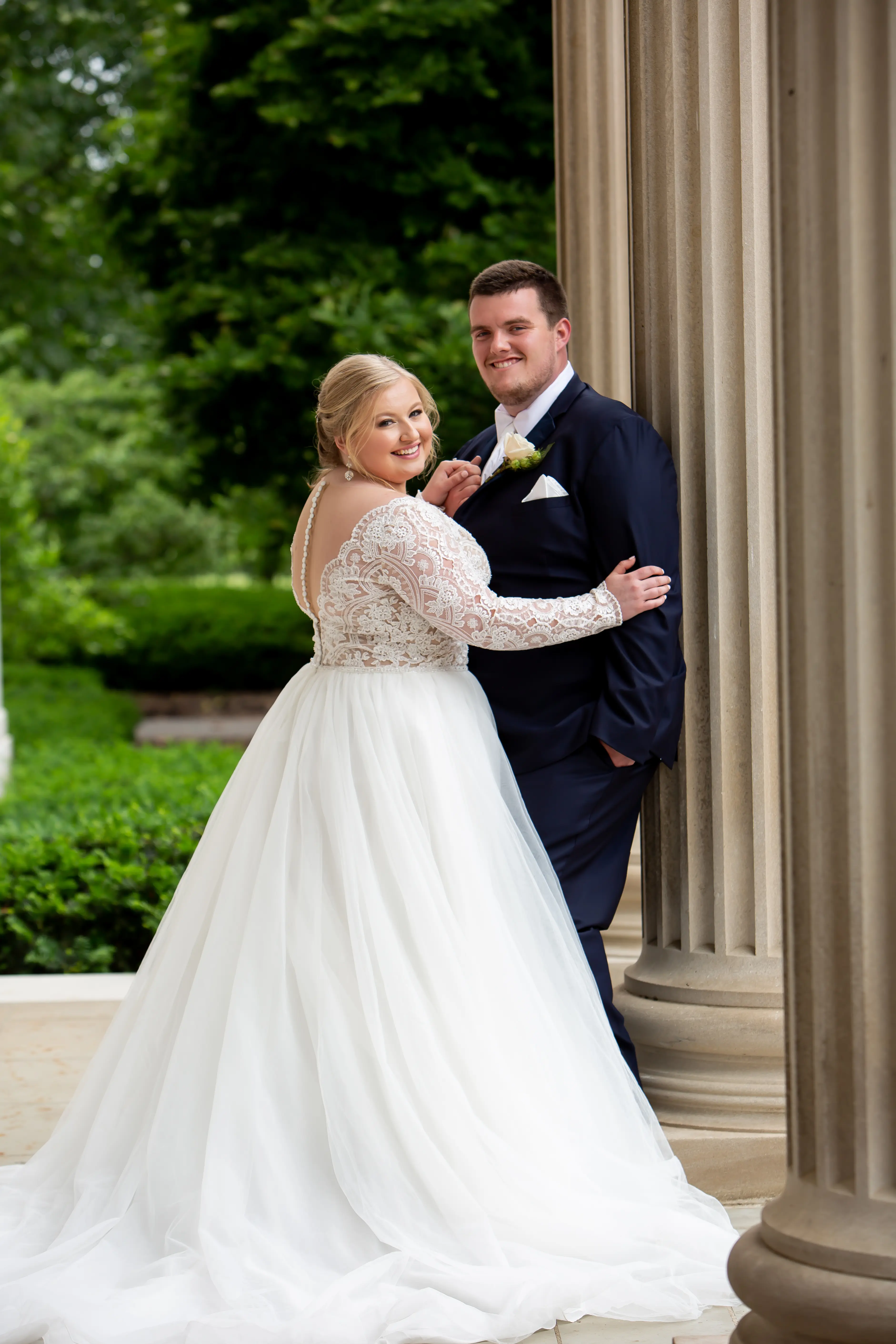 Bride and Groom Next to Tall Columns Wearing Wedding Dress Called Mallory Dawn by Maggie Sottero
