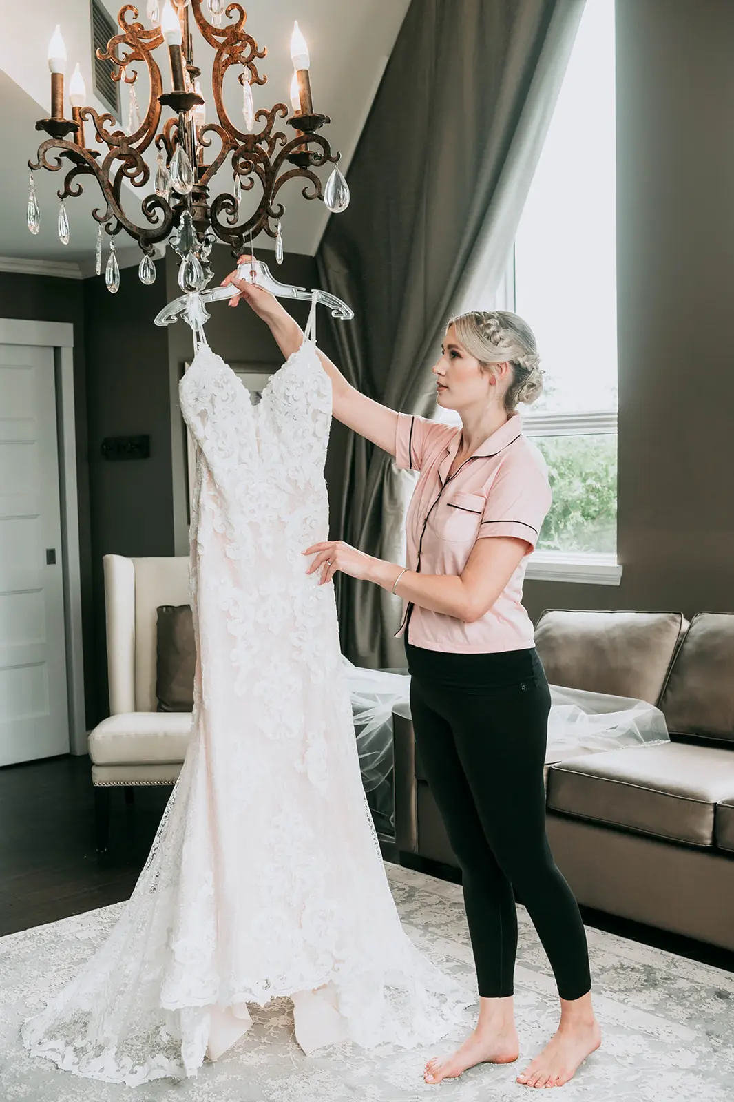 Bride hanging her wedding dress called Tuscany Lynette on a chandelier.