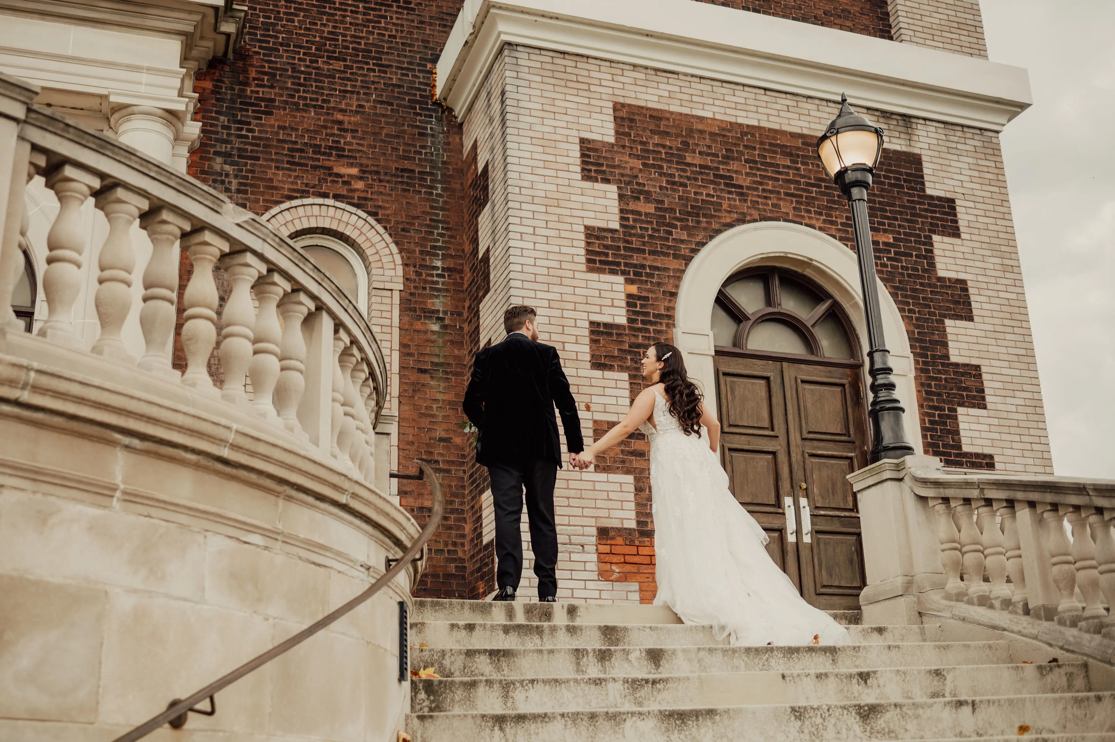 Bride Wearing Floral Lace Wedding Gown Called Laramie By Sottero And Midgley Walking Up Steps With Groom