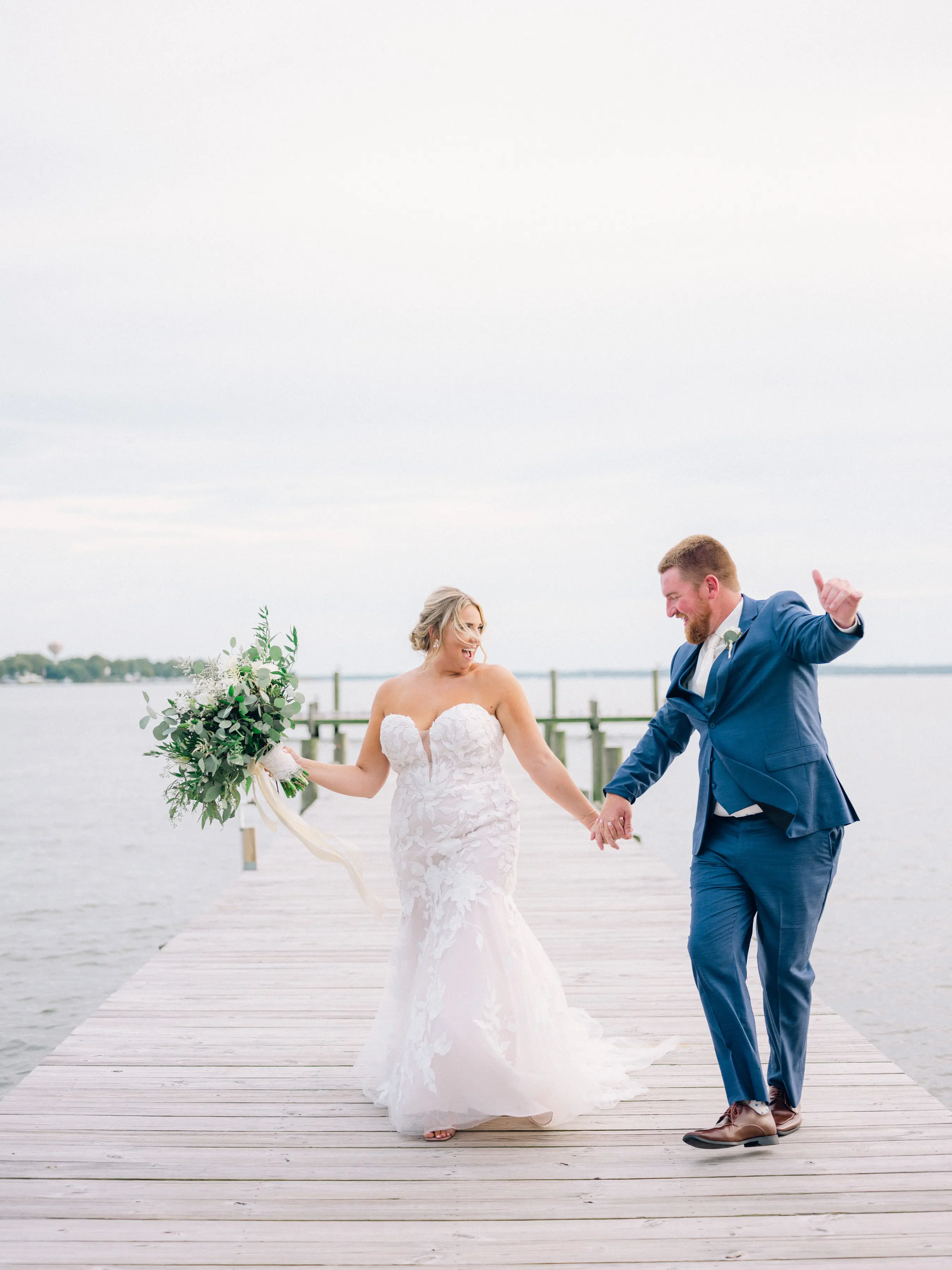 Bride Wearing Lace Mermaid Wedding Gown Called Hattie By Rebecca Ingram Walking With Groom Near A Lake