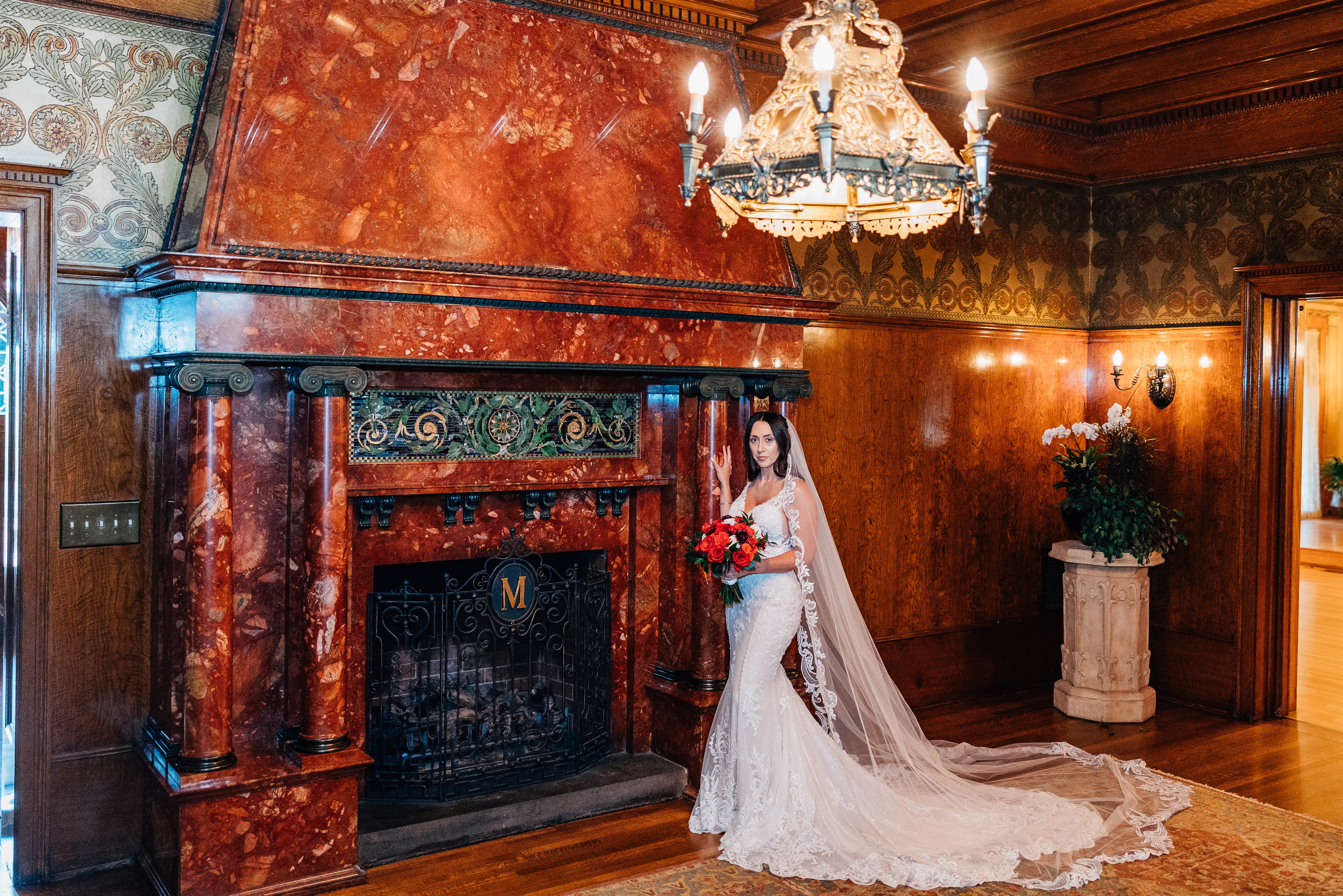Real Bride In Front Of Stone Fireplace Wearing A Fitted White Wedding Dress Named Veronique by Maggie Sottero