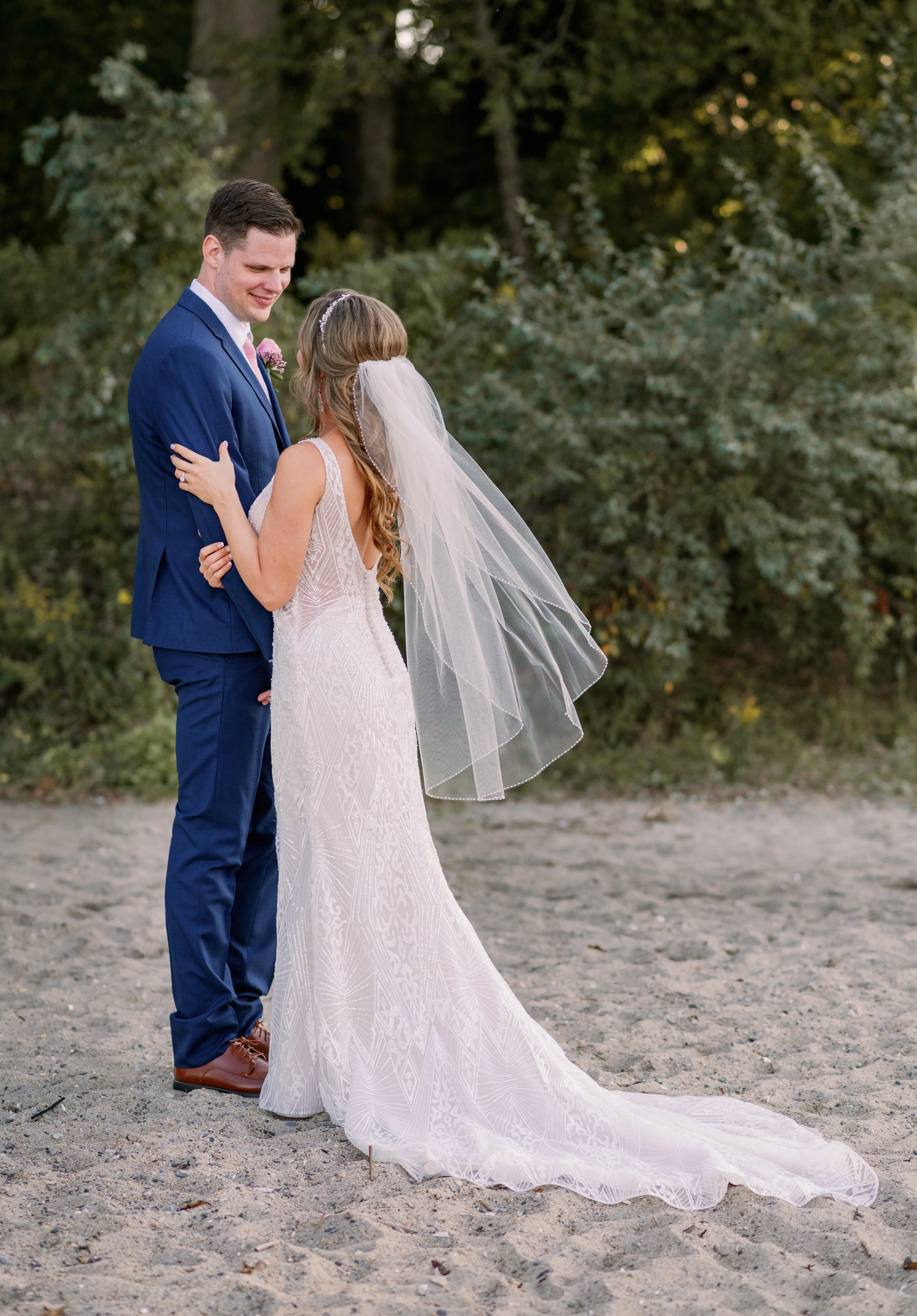 Bride and groom looking at each other stood on sand.