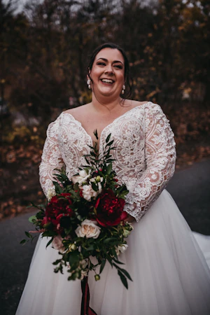 Plus Size Bride In Lace Long Sleeve Wedding Dress Called Mallory Dawn By Maggie Sottero Holding Red Bouquet