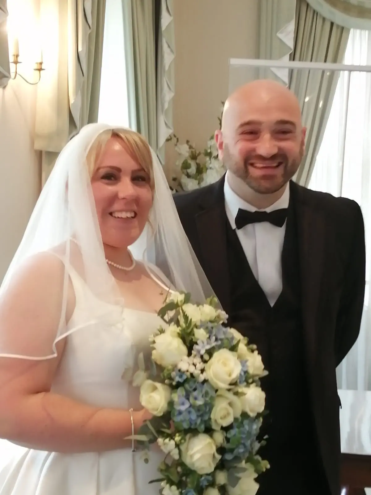 Bride wearing short veil holding ivory and soft blue bouquet smiling with her groom.