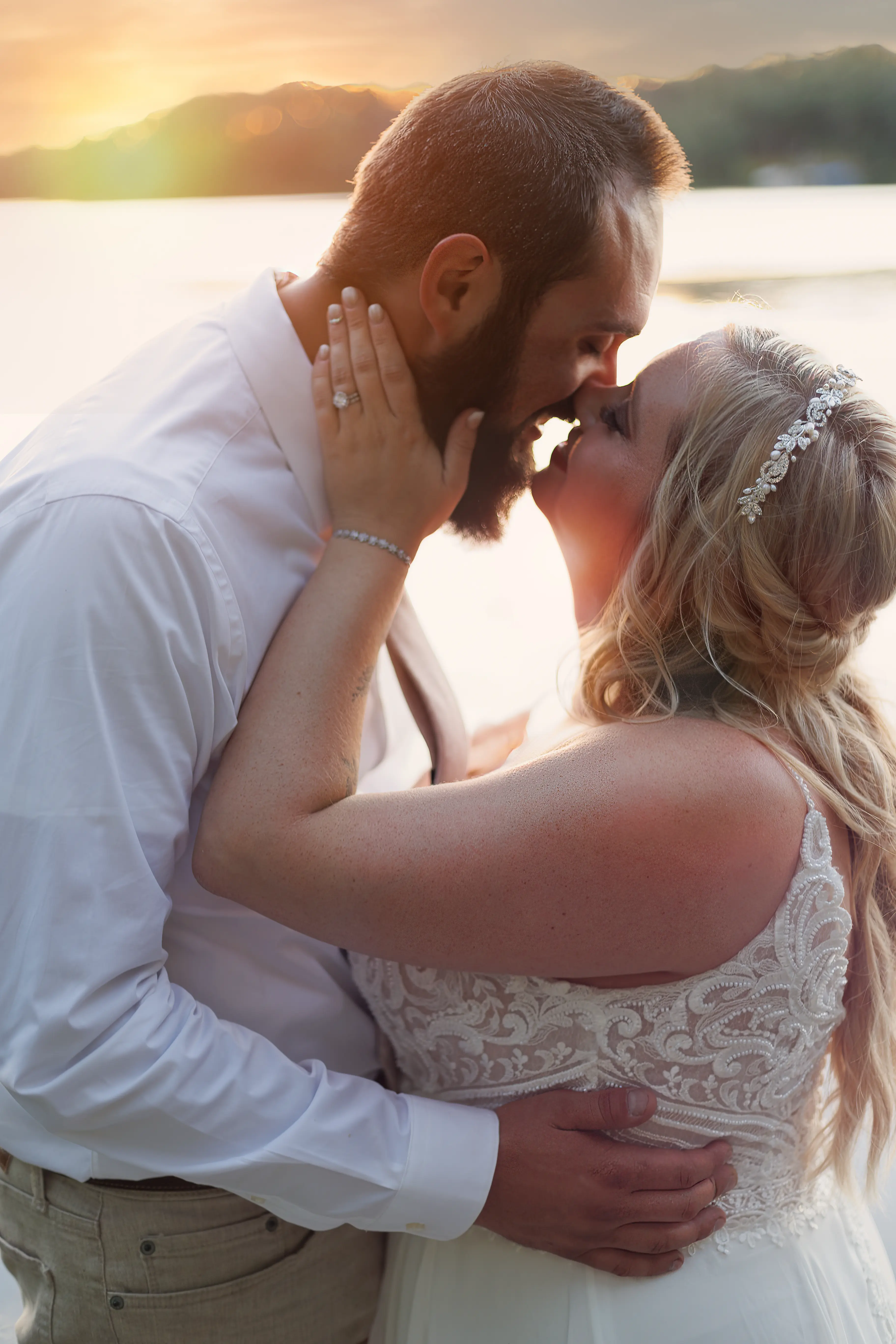Bride Wearing Beaded Wedding Dress With Flowy Skirt Called Lorraine By Rebecca Ingram Kissing Groom At Sunset