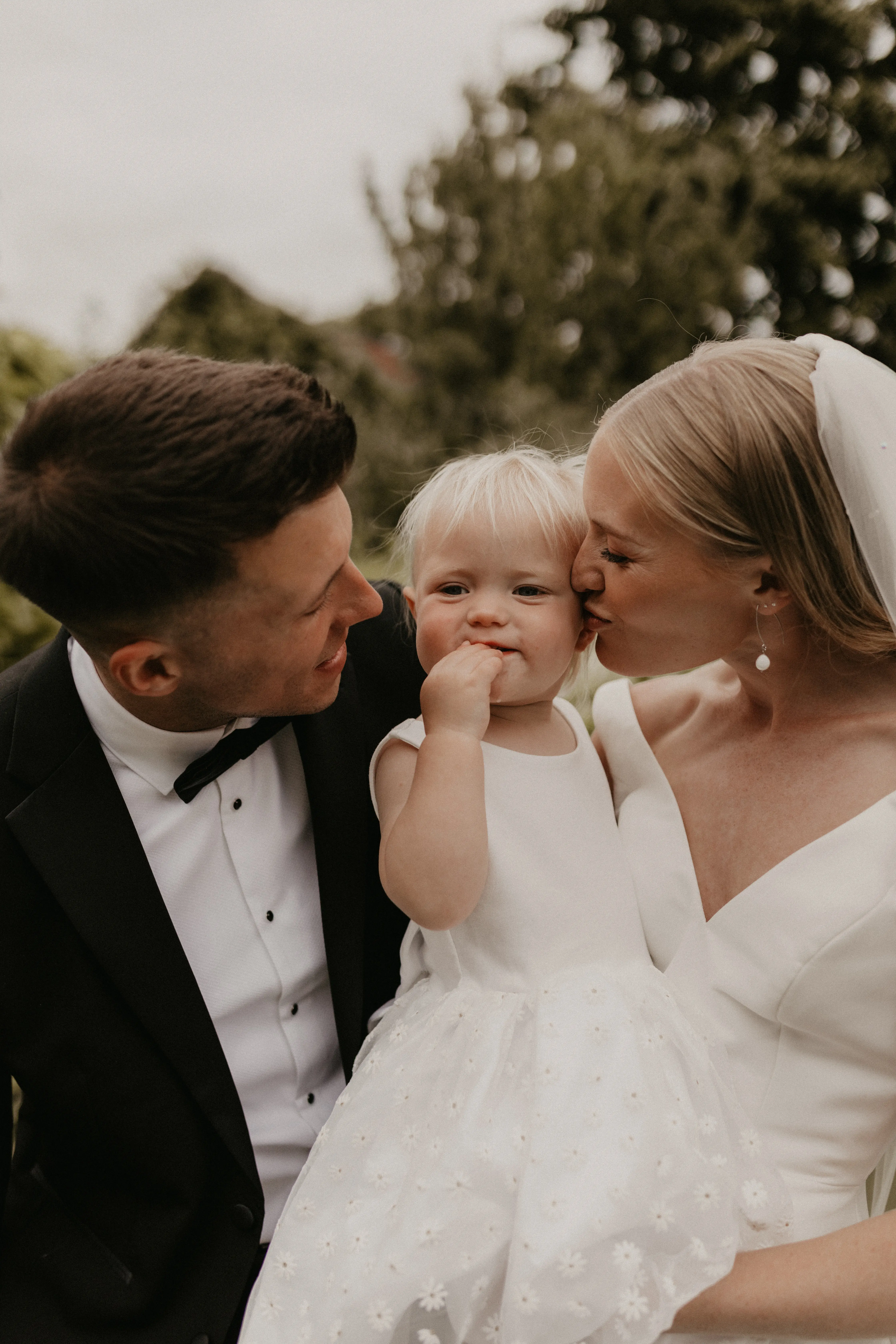 Bride wearing Paxton by Maggie Sottero and her husband kissing a child