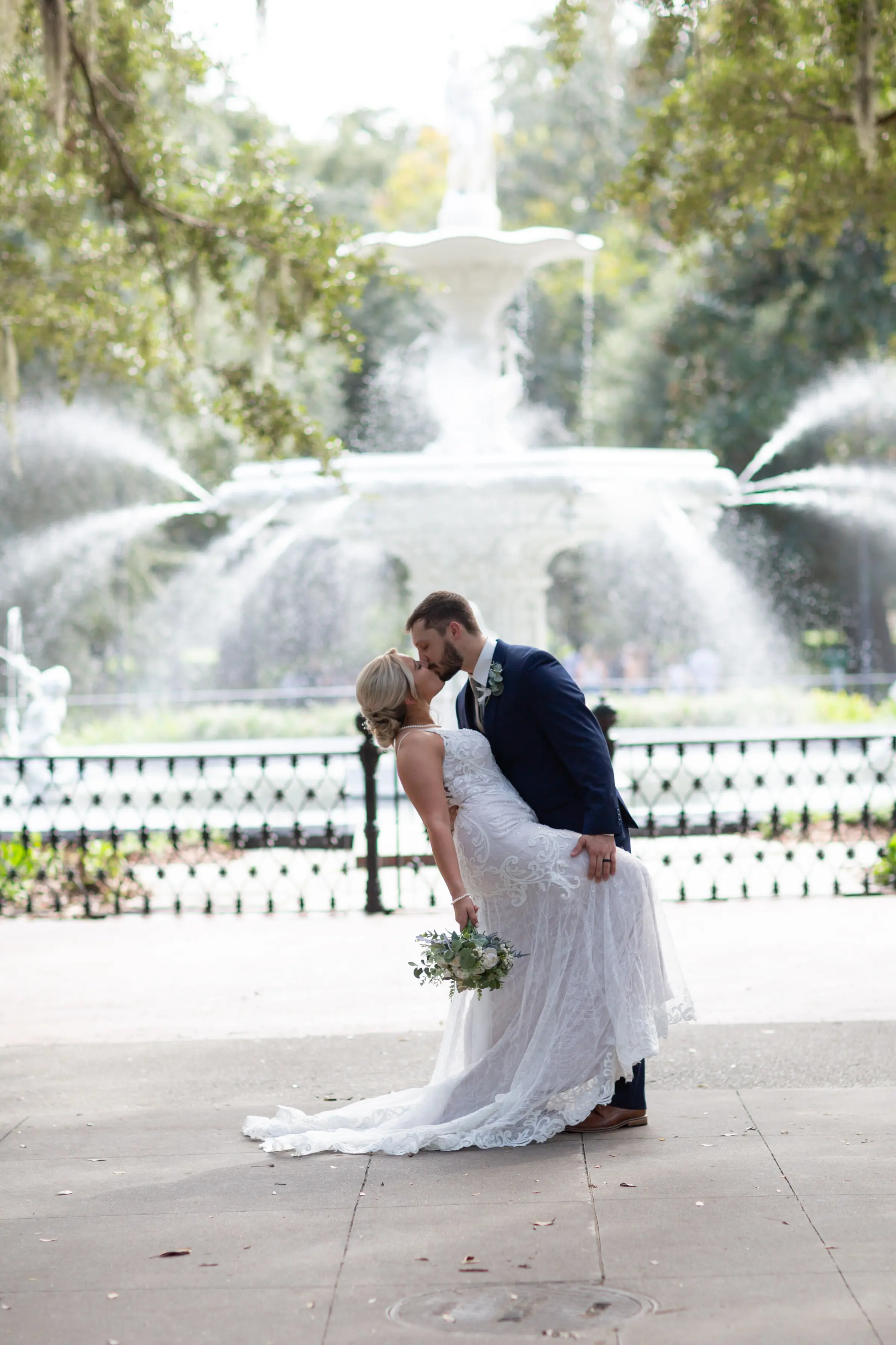 Bride and groom kissing by huge fountain.