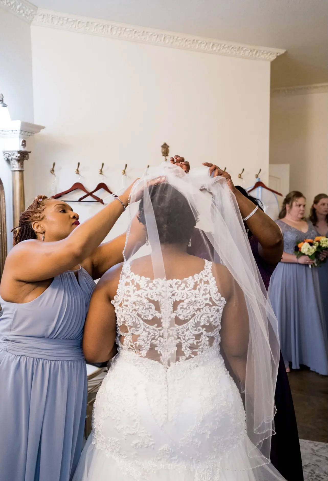 Bridesmaids putting the veil on the bride wearing wedding dress called Veda.