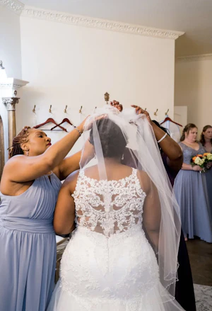 Bridesmaids putting the veil on the bride wearing wedding dress called Veda.