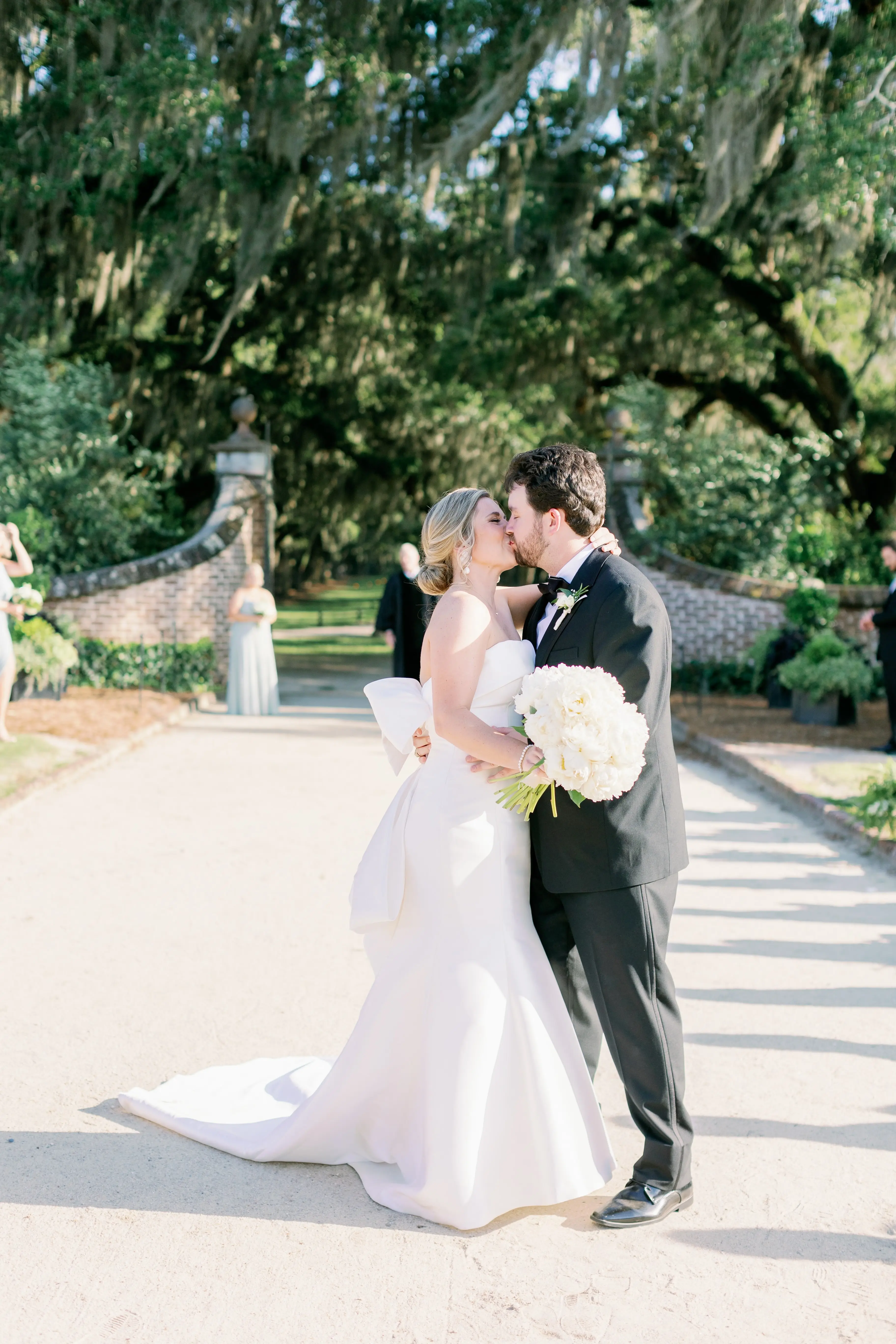 Bride with groom wearing strapless elegant mermaid wedding dress outdoors holding flower bouquet.