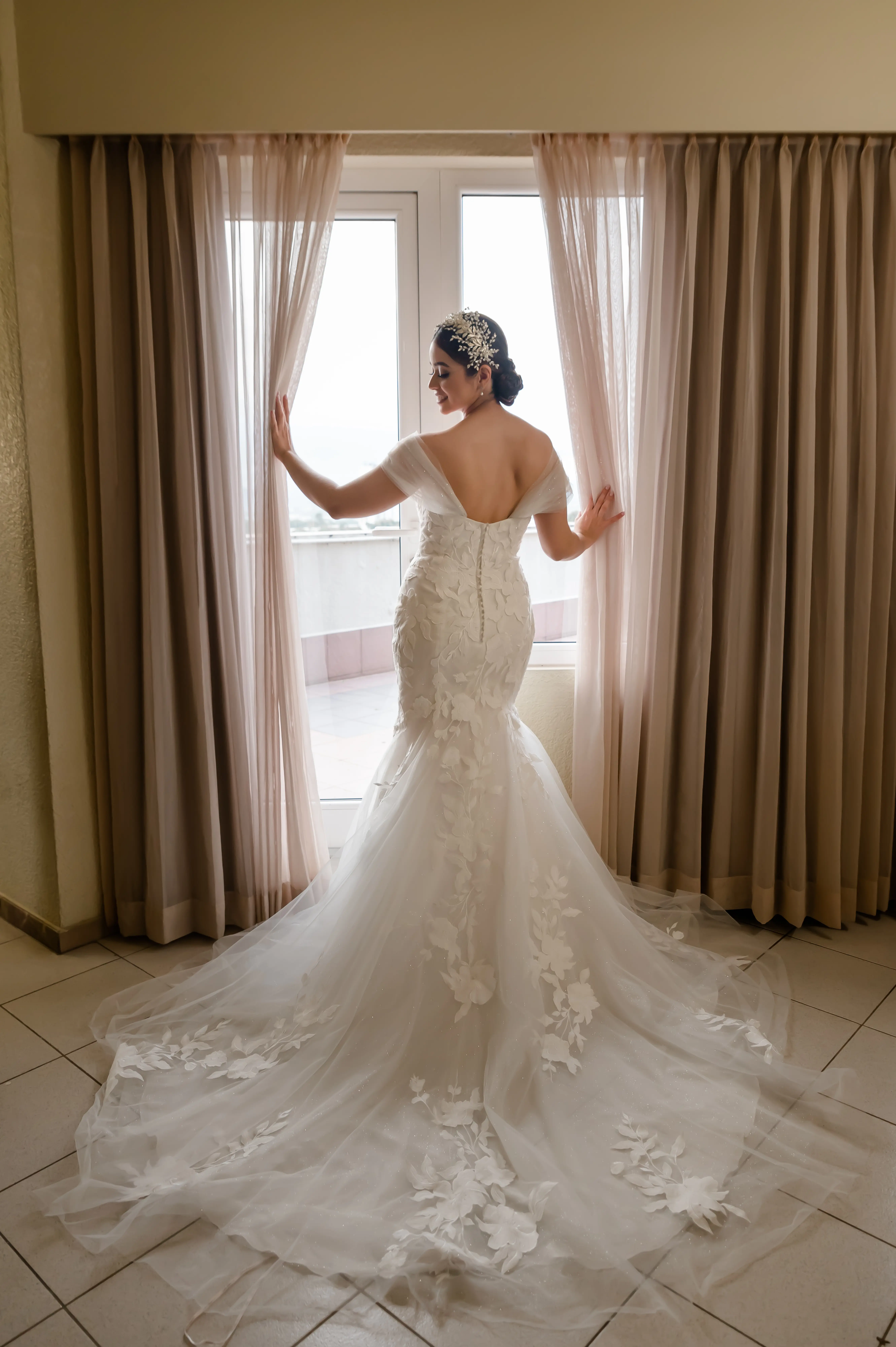 Bride Standing by Window Showing Train on Wedding Dress Called Hattie by Rebecca Ingram