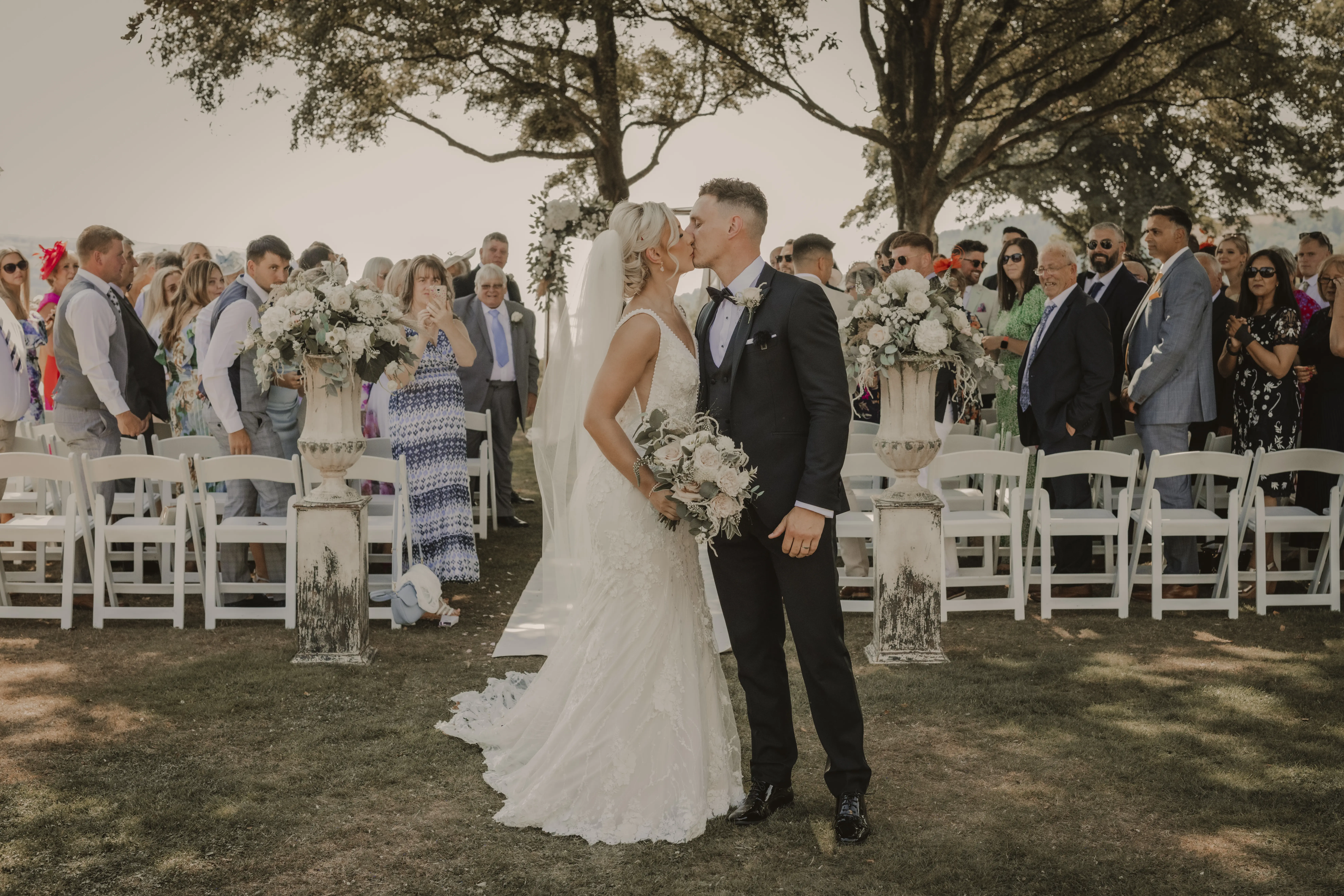 Newlyweds Kiss. Bride in Vintage-Inspired Mermaid Wedding Dress with 3-D Floral Motifs and Extended Scalloped Lace Train Called Cruz by Sottero & Midgley