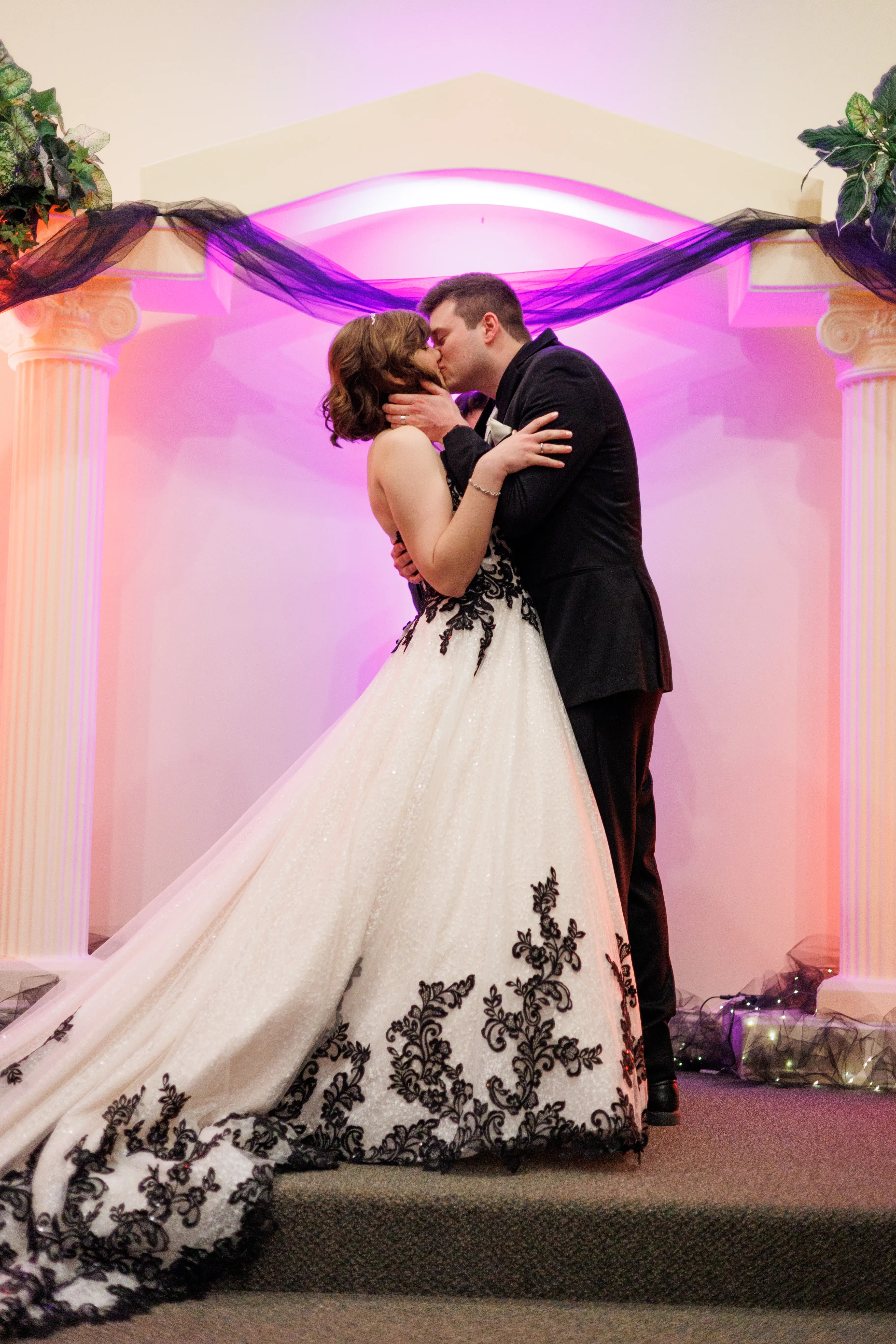 Bride And Groom Share Kiss At The Altar. Bride Wearing Black And White Lace Strapless Ball Gown Called Tristyn By Maggie Sottero
