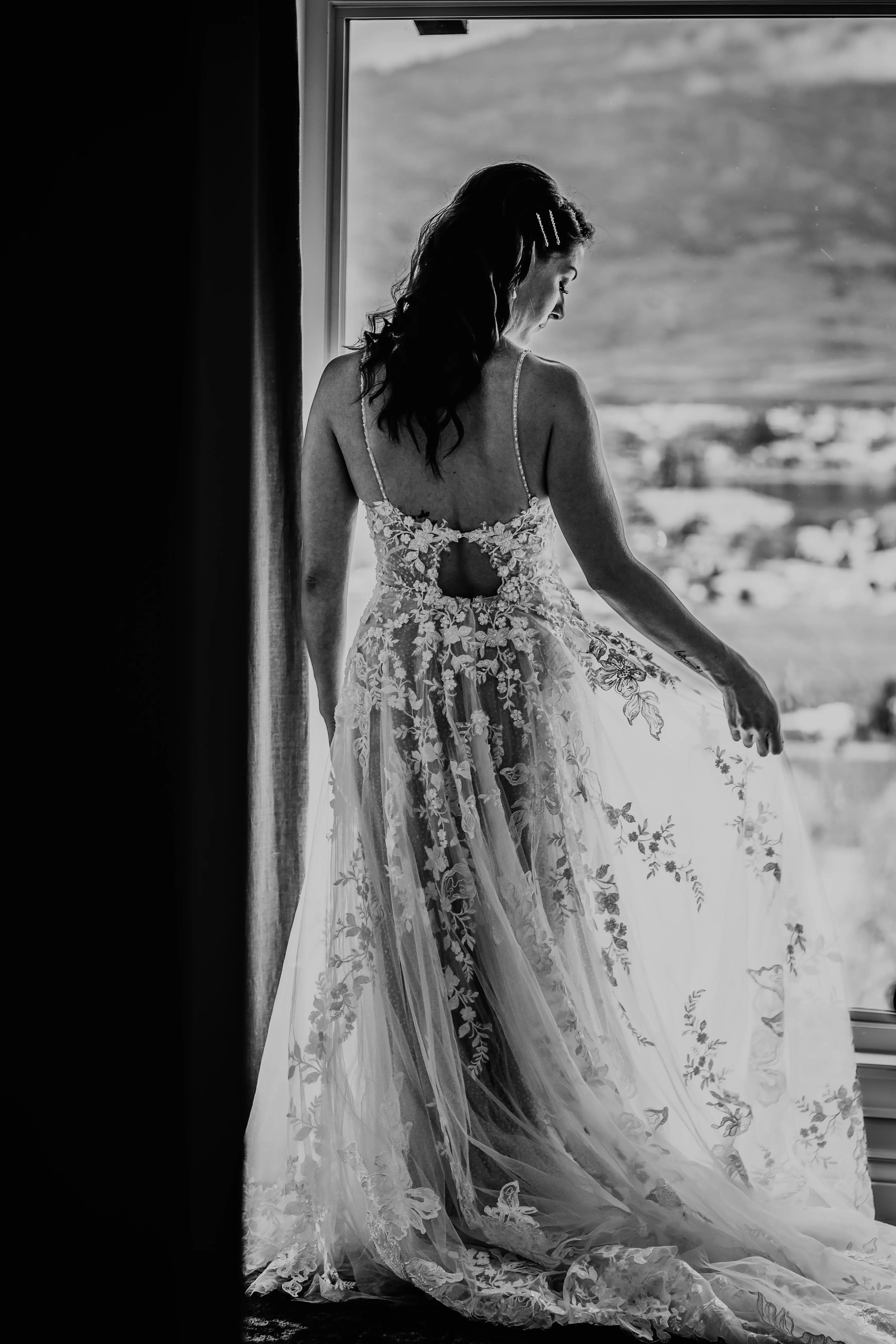 Bride Wearing Romantic Key Hole Back A-Line Wedding Dress Called Marlow By Maggie Sottero Admires Lace By A Window