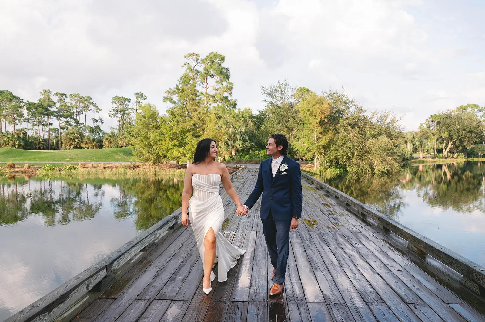 Bride Wearing Grecian Inspired Wedding Dress Called Gabrielle By Maggie Sottero Walking On A Boardwalk With Groom