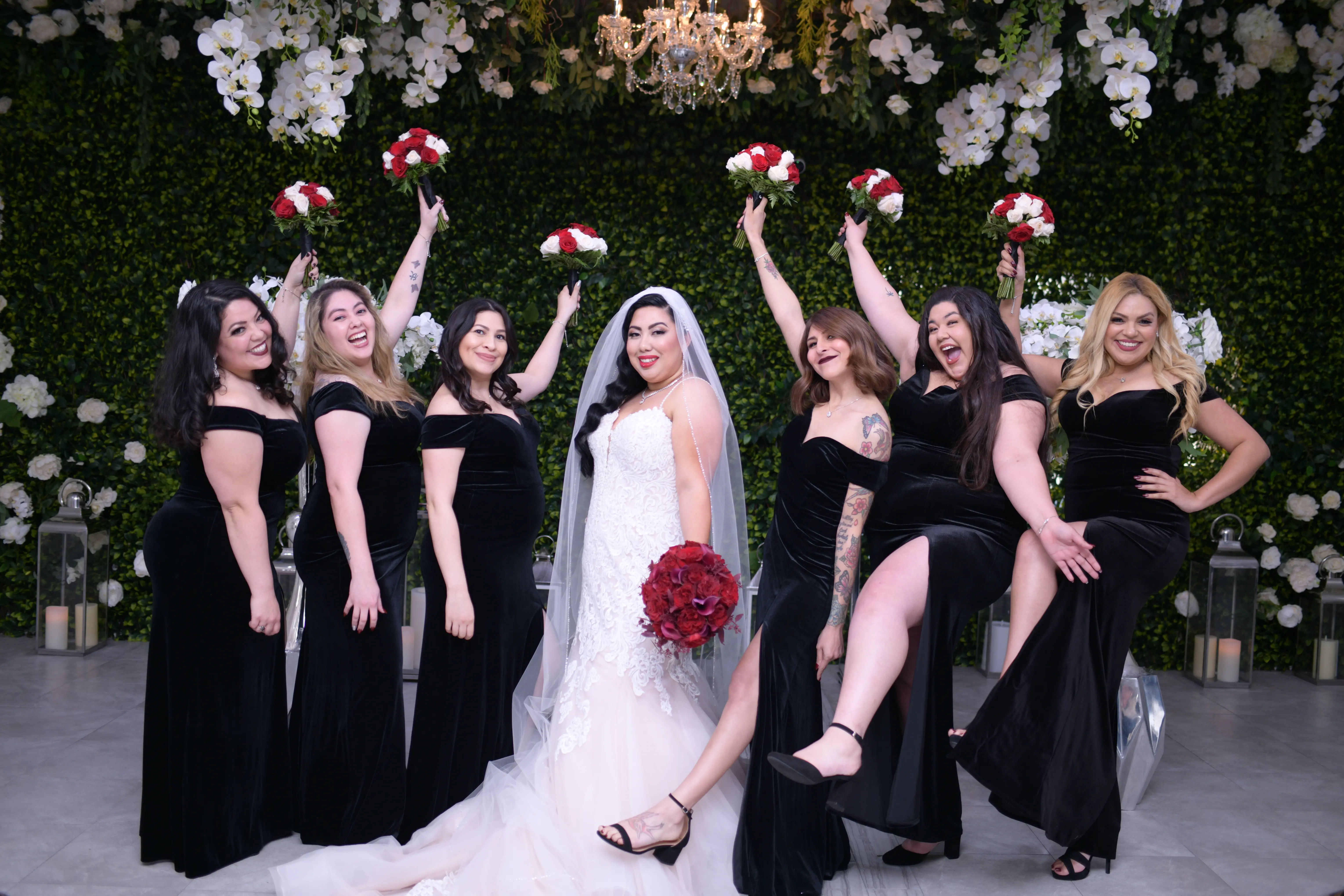 Bride with her bridesmaids wearing black dresses and with red and white bouquets.