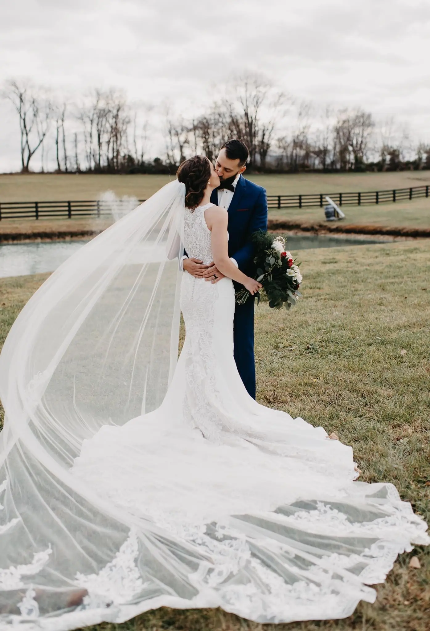 Bride and Groom Kiss With Veil Flowing Behind. Bride Wearing Lace Detailed Halter Wedding Dress Called Kevyn By Sottero And Midgley