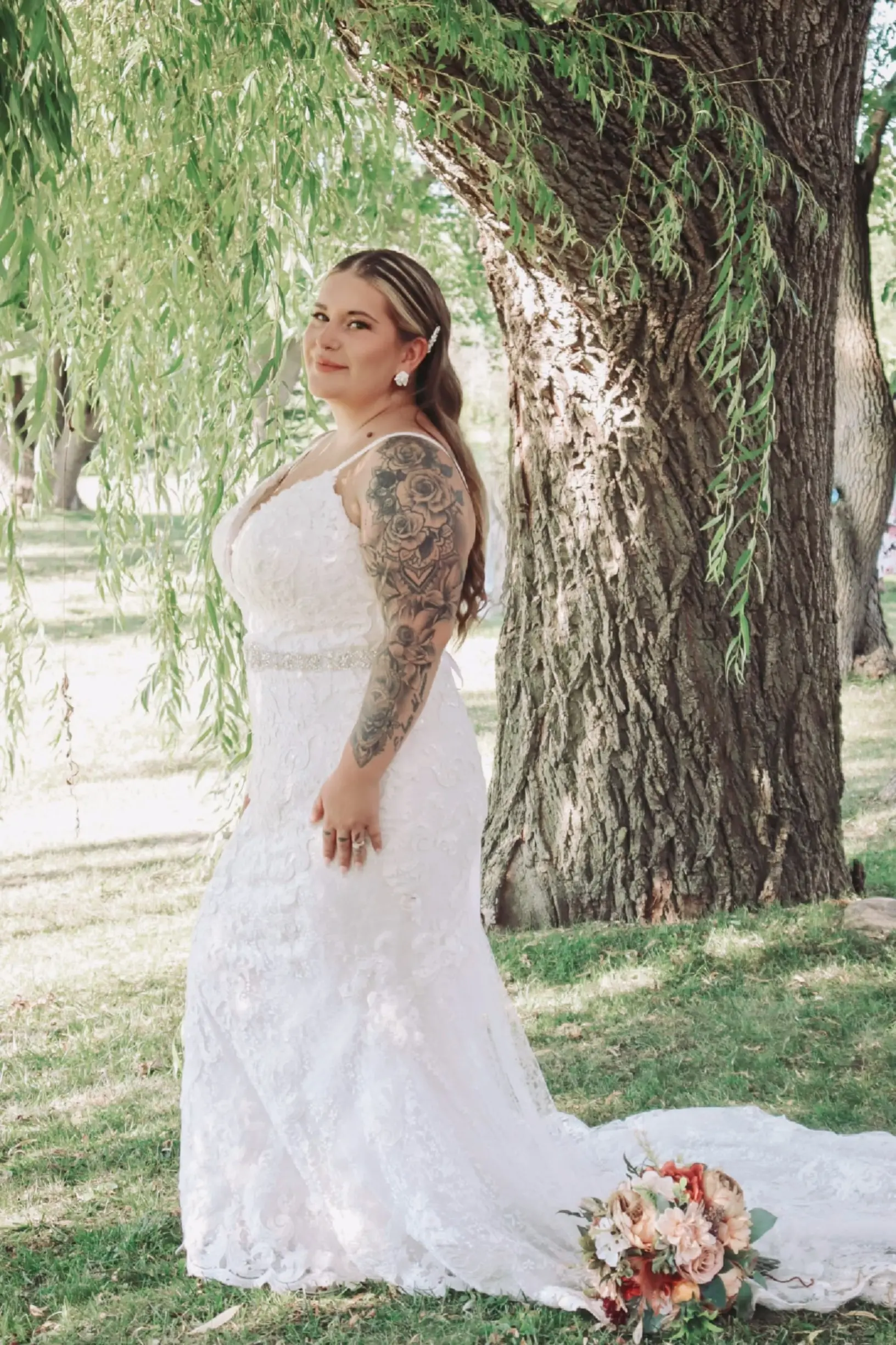 Bride Wearing Sheath Lace Wedding Dress With Beaded Belt Called Tuscany Lynette By Maggie Sottero Posing With Flower Bouquet