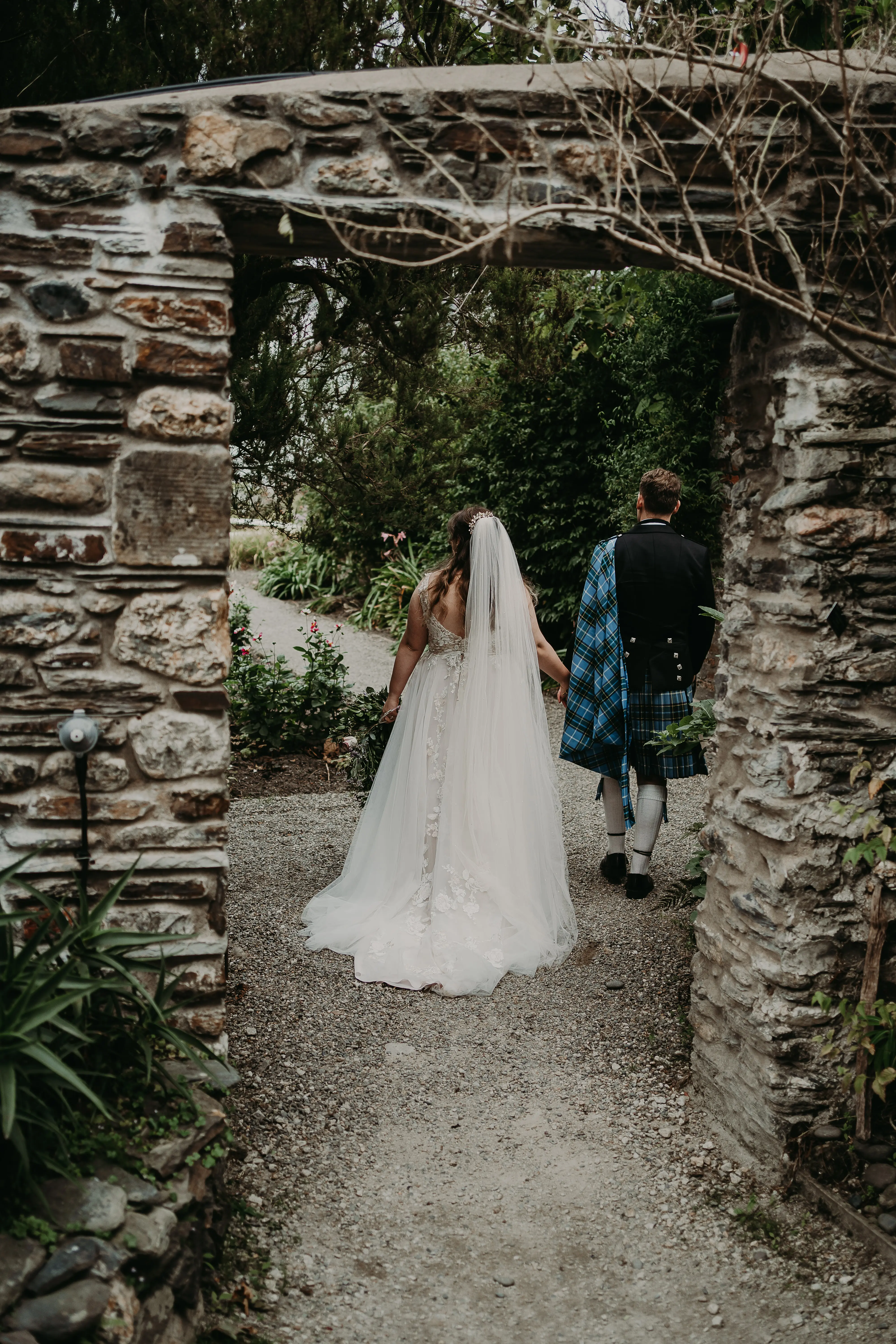 Newlyweds walking hand in hand on a garden path.