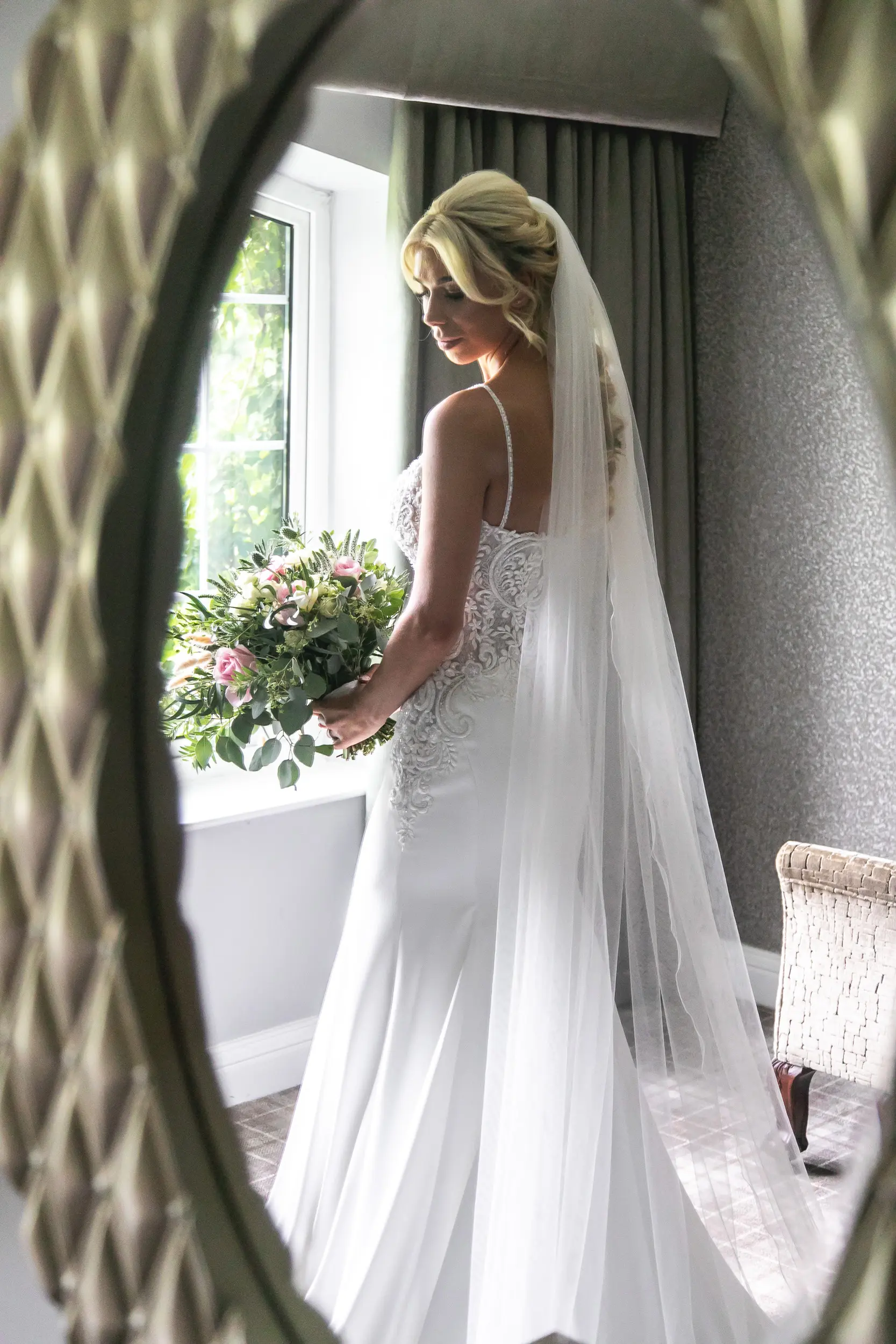 Bride holding leafy bouquet with pink flowers wearing wedding dress called Juanita.
