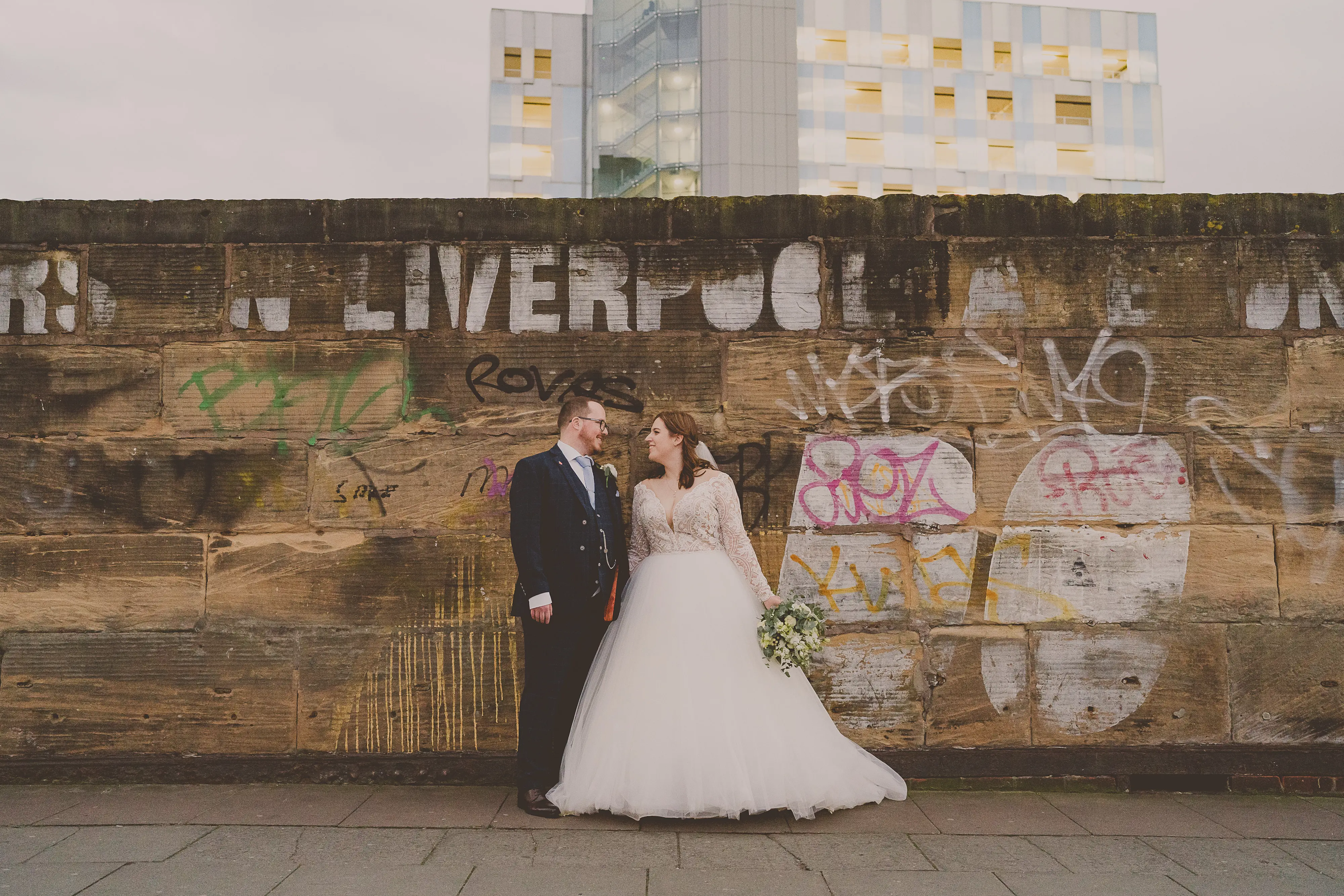 Bride And Groom Standing Together. Bride Wearing Lace Long Sleeve Ball Gown Wedding Dress With Tulle Skirt Called Mallory Dawn By Maggie Sottero