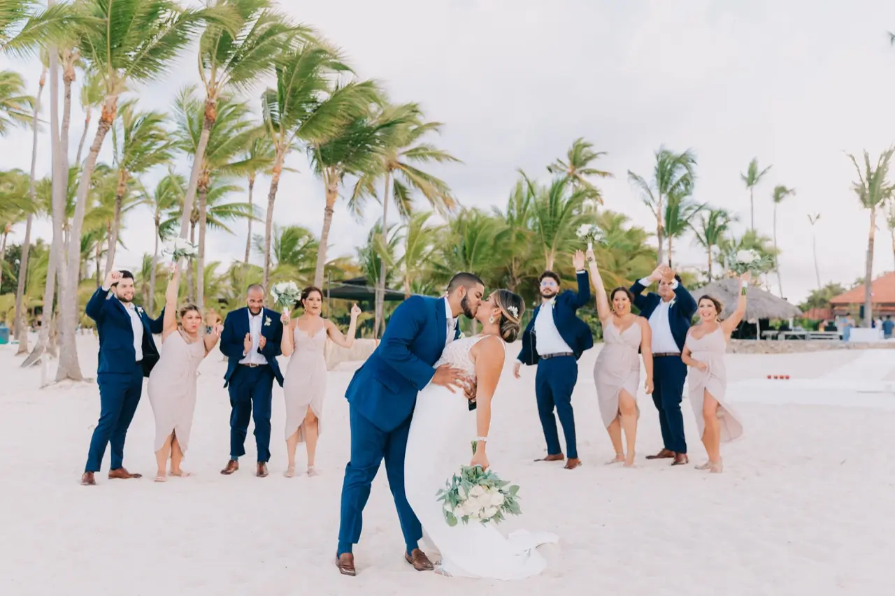 Groom dipping bride for a kiss while wedding party cheers.