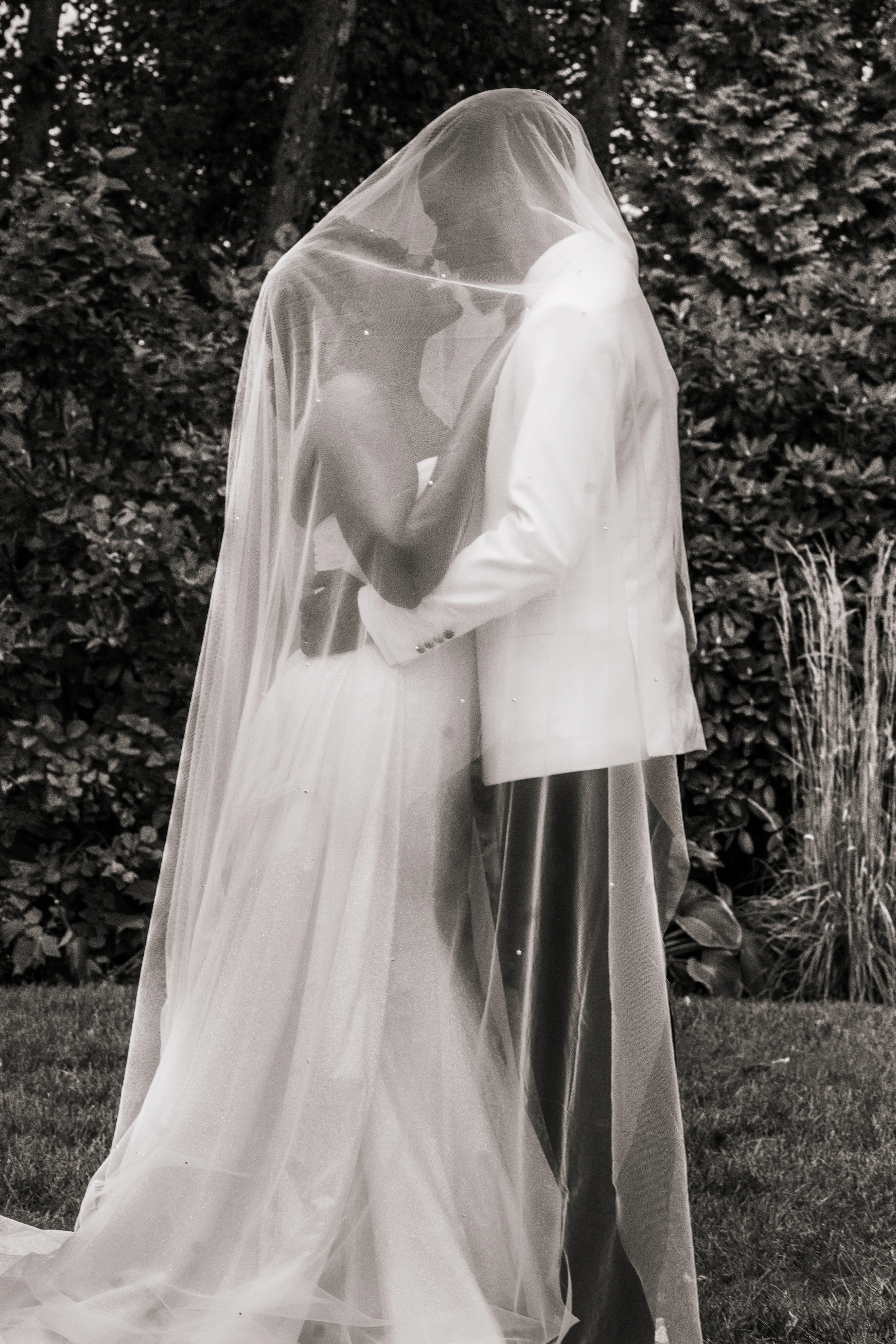 Bride Wearing Simple Fit and Flare Wedding Dress Called Anniston Lane Kissing Groom Underneath Her Veil